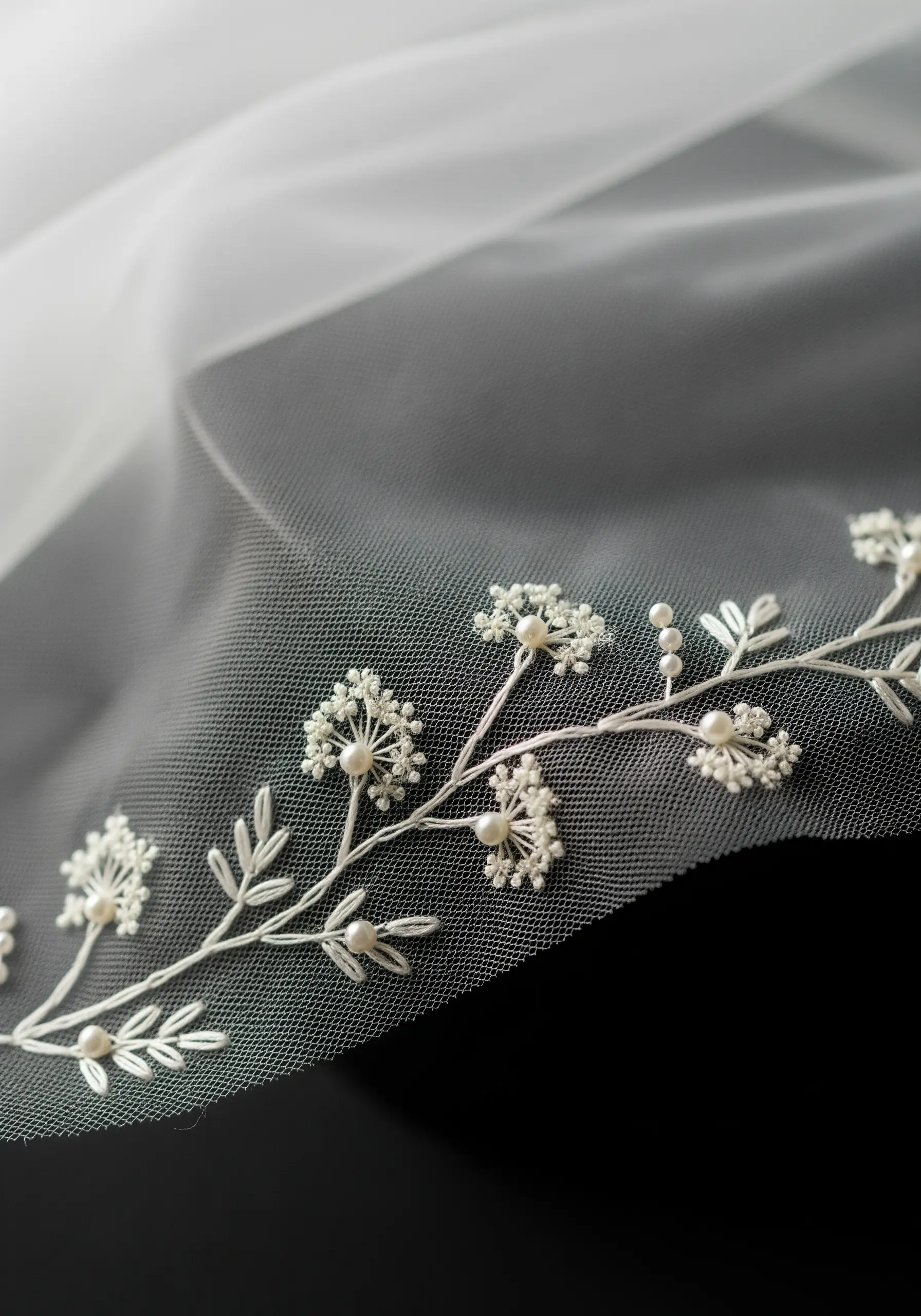 A close-up of a sheer white veil with delicate embroidery of flowers made from thread and pearls.