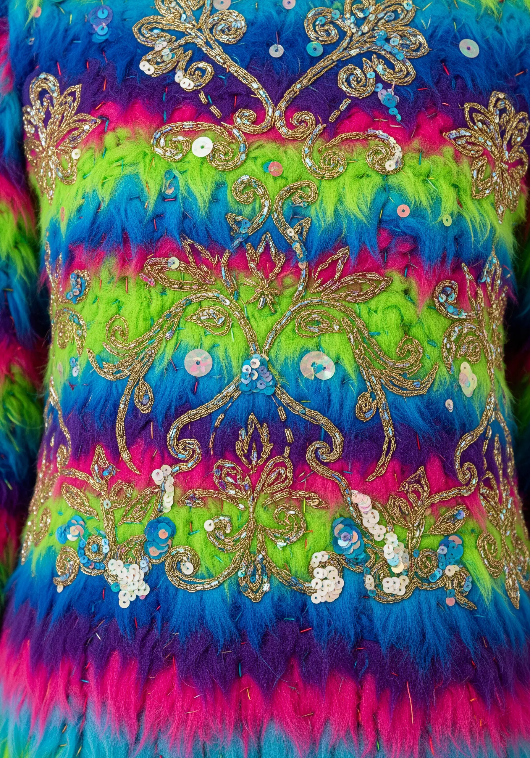 A close-up of a brightly colored faux fur garment heavily embellished with goldwork embroidery and sequins.