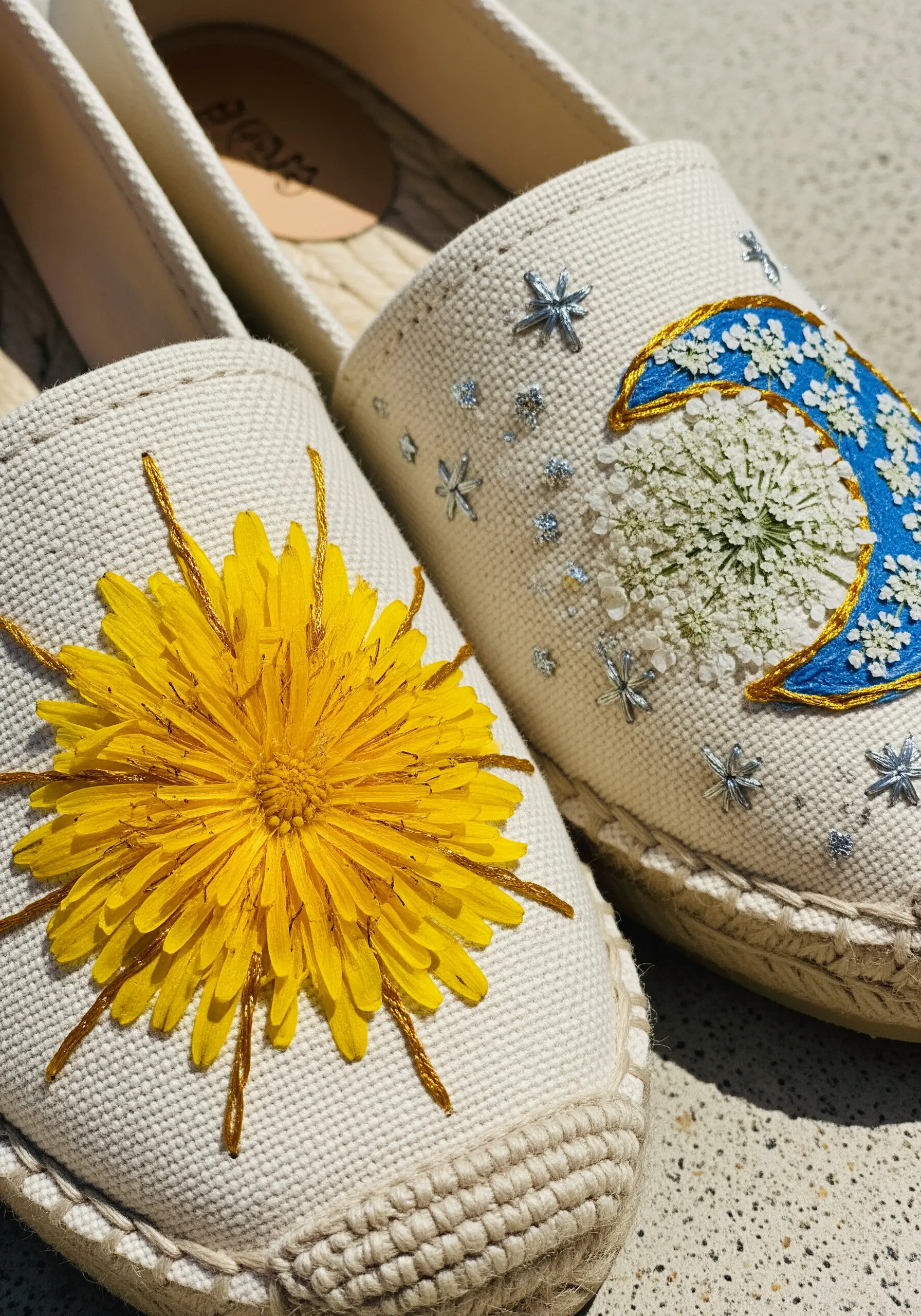 A pair of espadrilles, one embroidered with a sun and dandelion, the other with a moon and flowers.