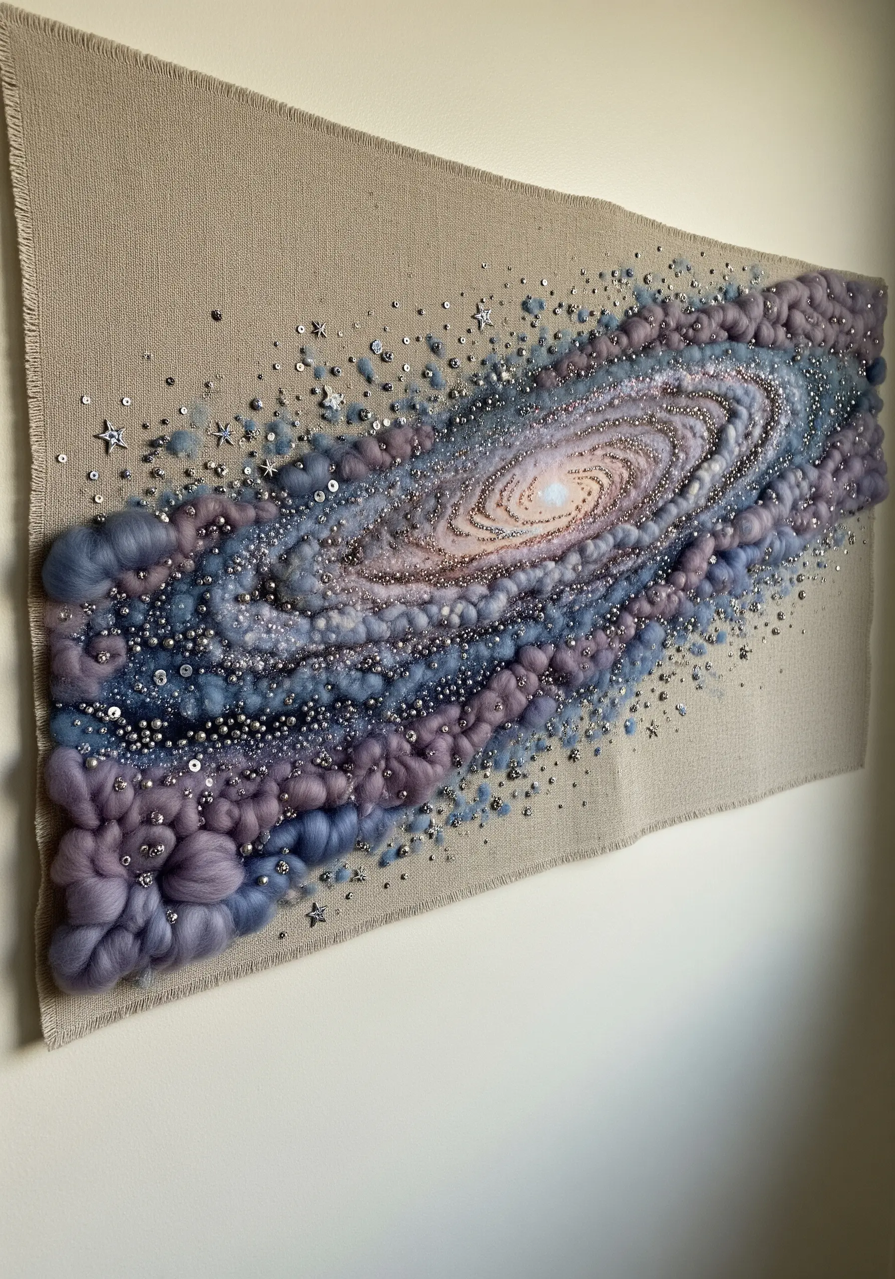 A large textile wall hanging of a spiral galaxy made with wool roving, beads, and sequins.