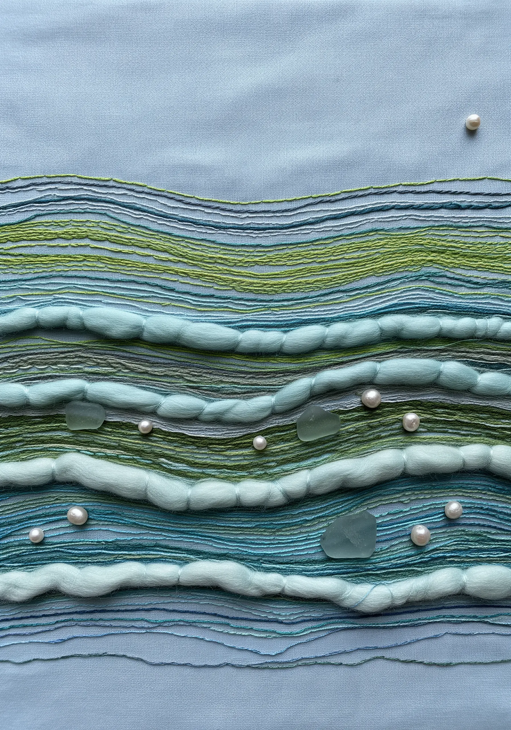 A seascape textile made with wool roving, with real sea glass and pearls stitched in.