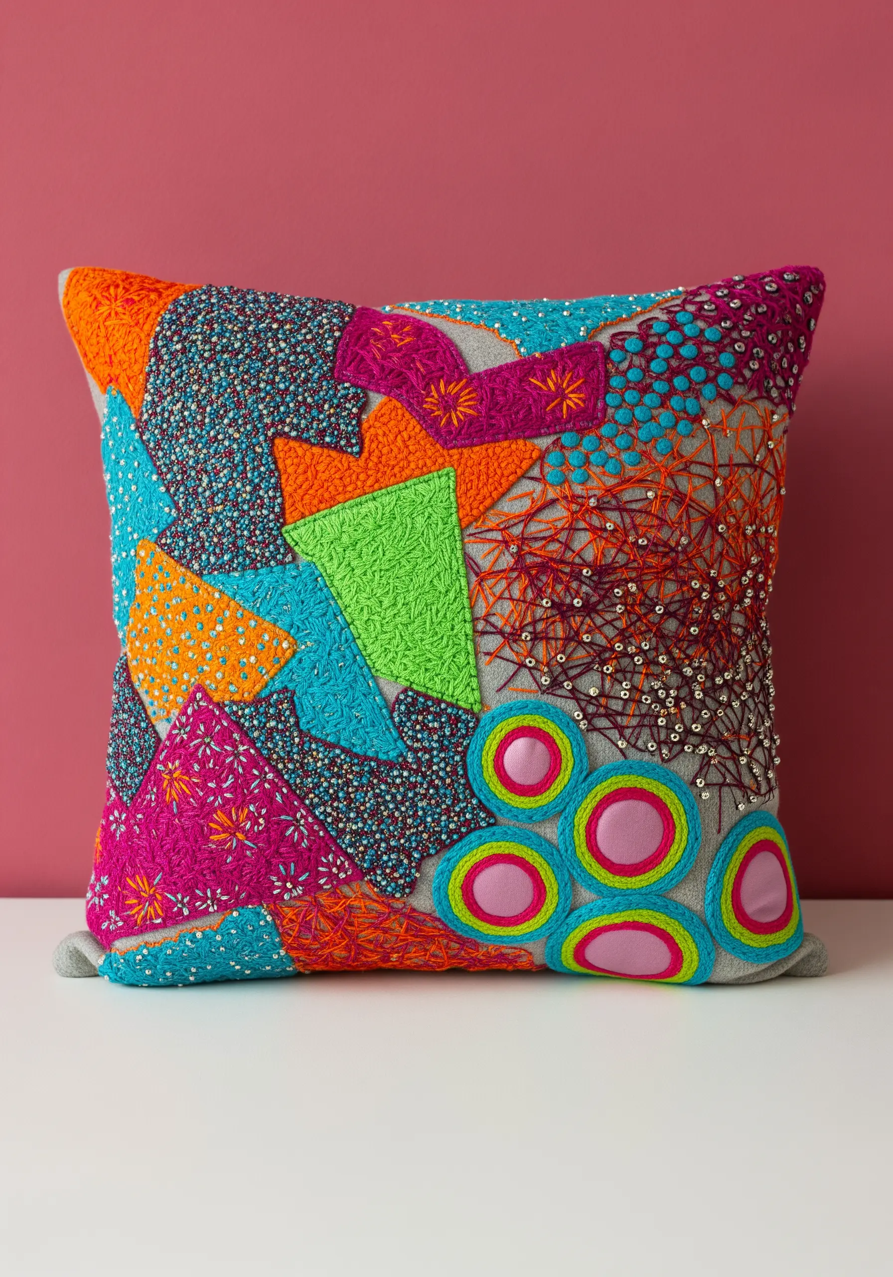 A brightly colored pillow covered in a collage of appliqué, beads, sequins, and embroidery.