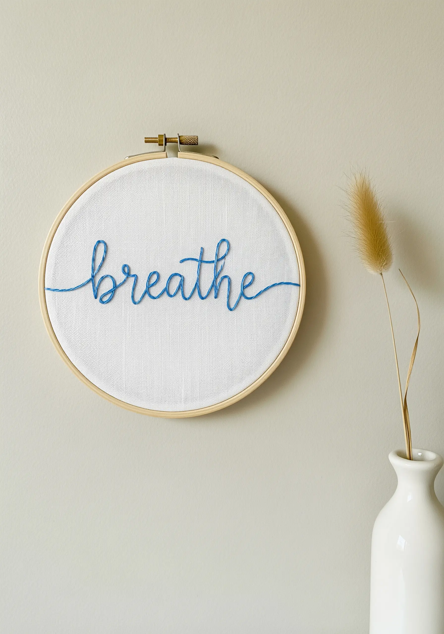 The word 'breathe' in fine blue cursive stem stitch on white fabric.