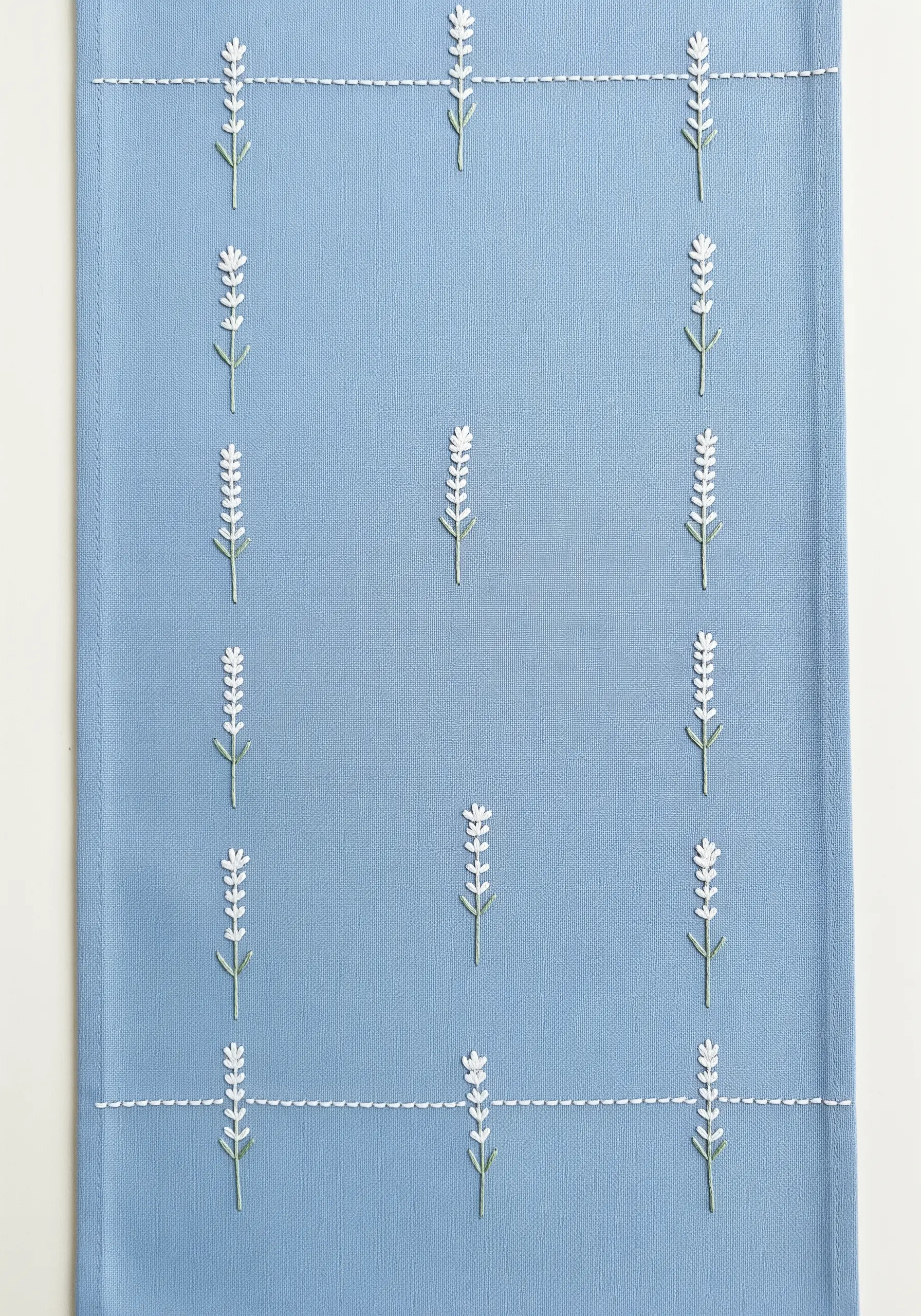 A blue table runner with a pattern of tiny, minimalist white lavender sprigs in a grid.