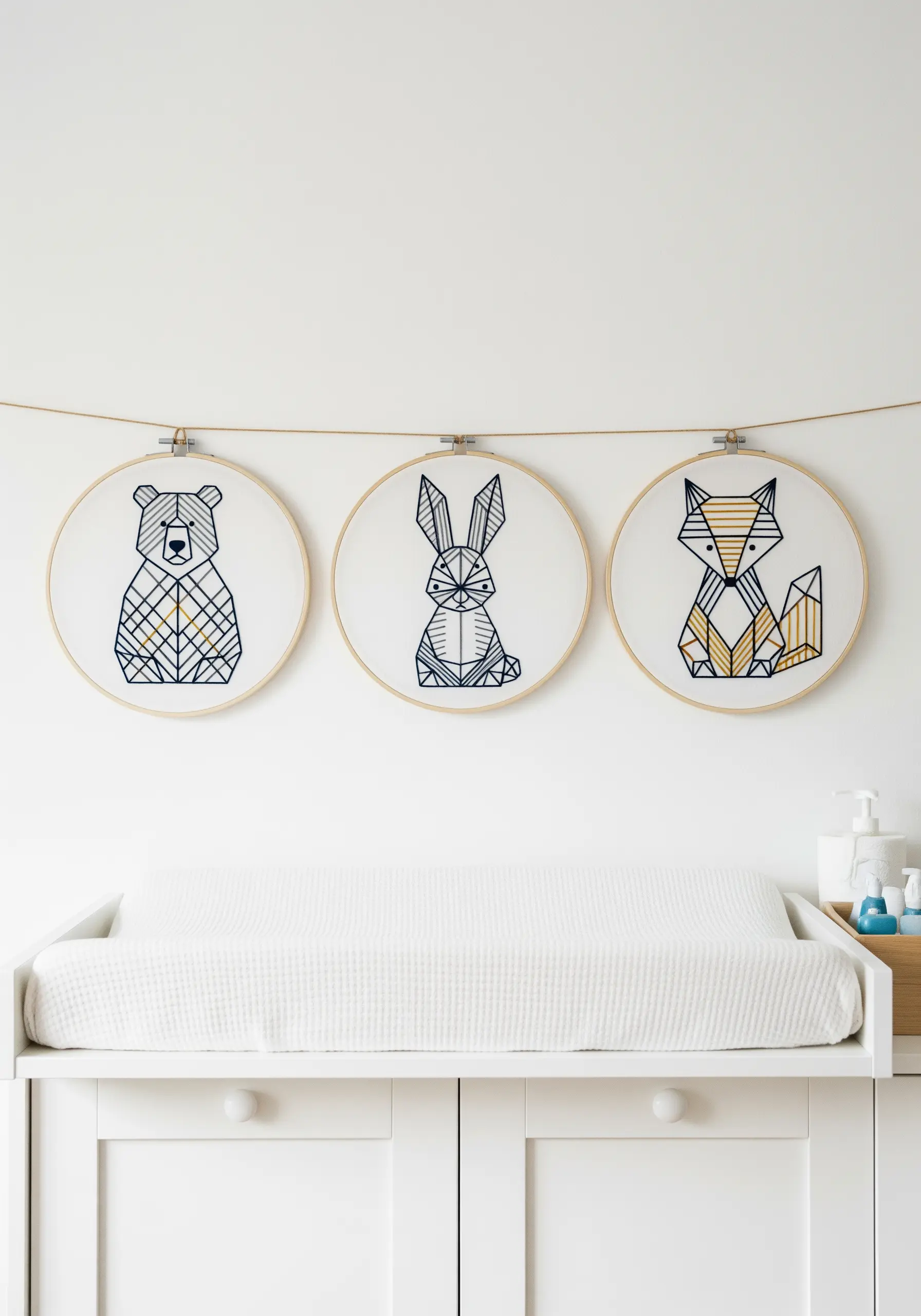 Three embroidery hoops displaying geometric line art of a bear, rabbit, and fox.