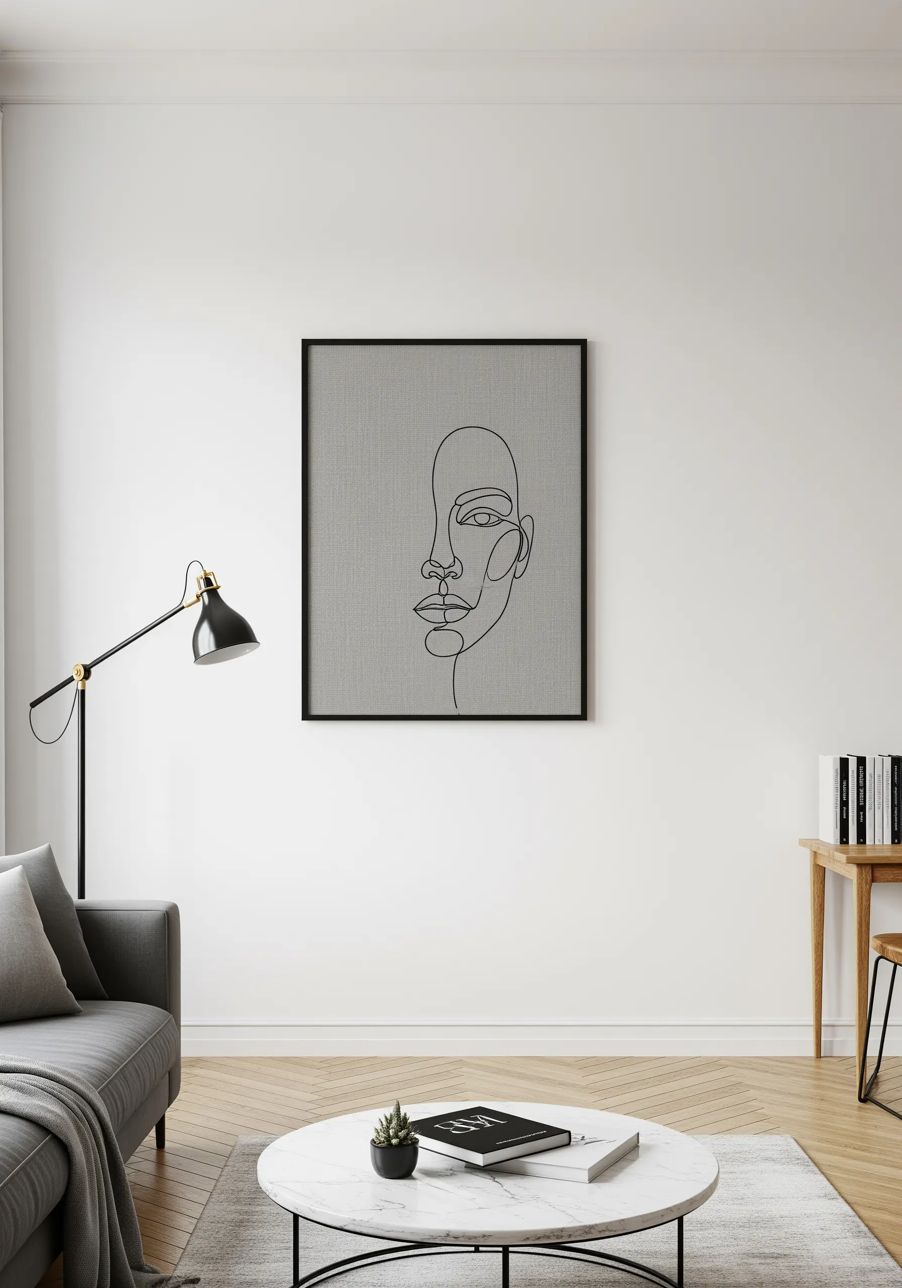 A framed, single-line embroidered portrait of a face on a gray fabric in a minimalist room.