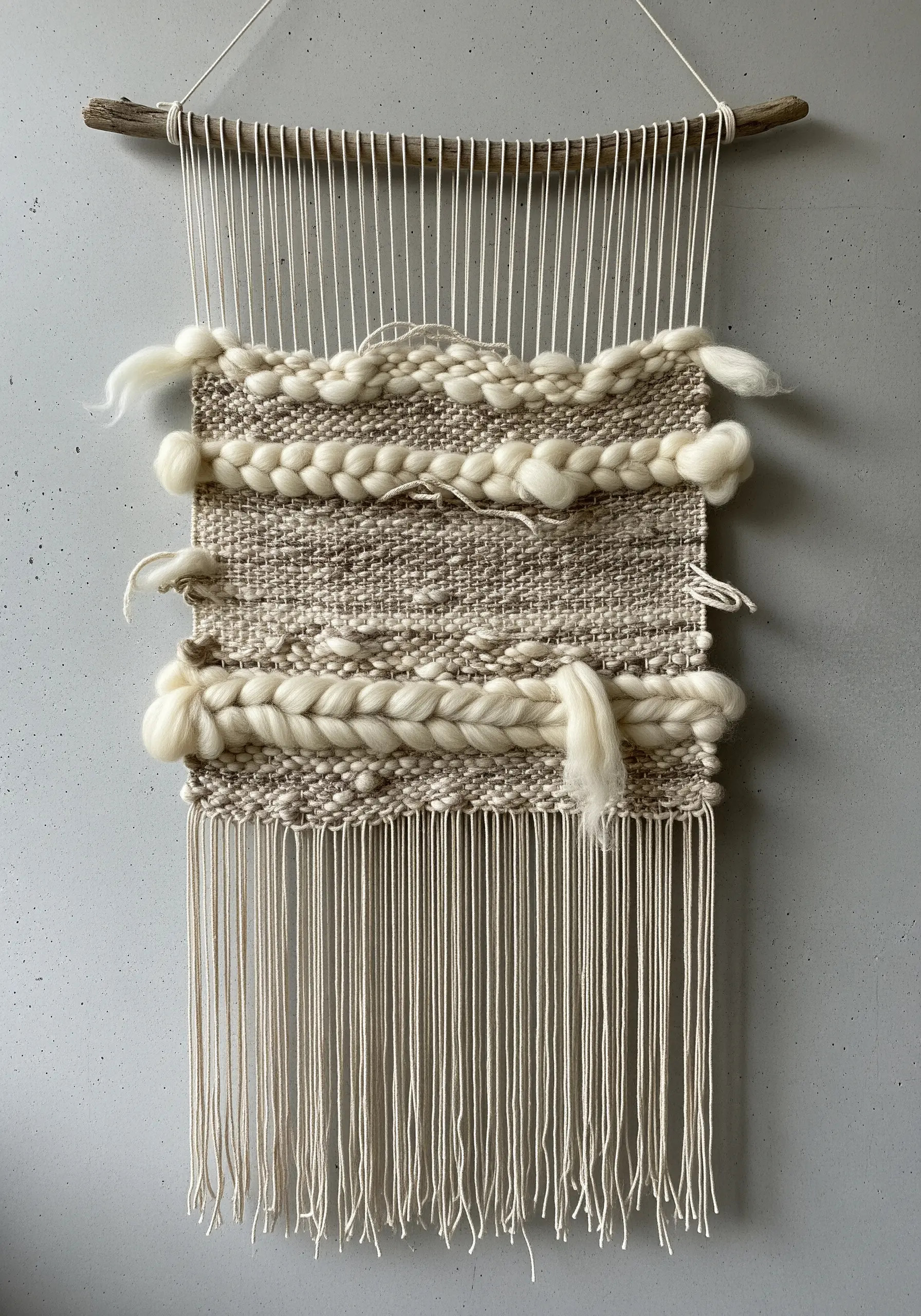 A rustic woven wall hanging with chunky wool roving and mixed textures on a natural branch.
