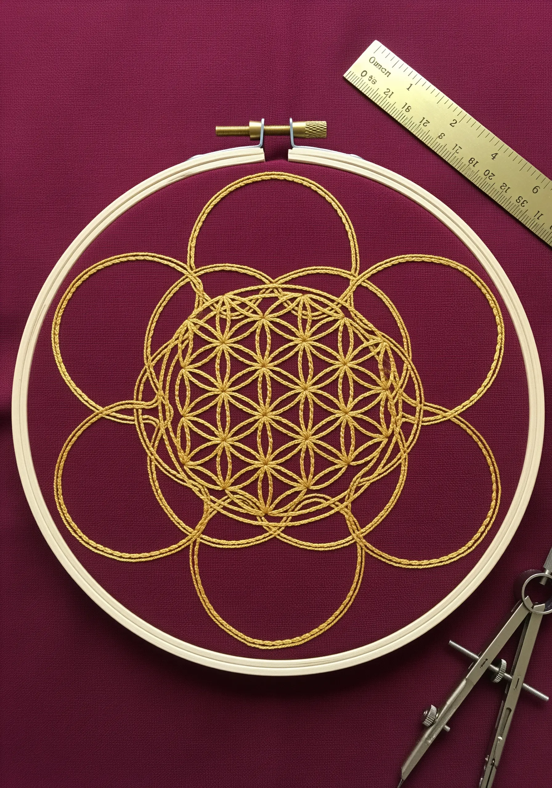 The Flower of Life sacred geometry pattern stitched in gold thread on burgundy fabric using couching.