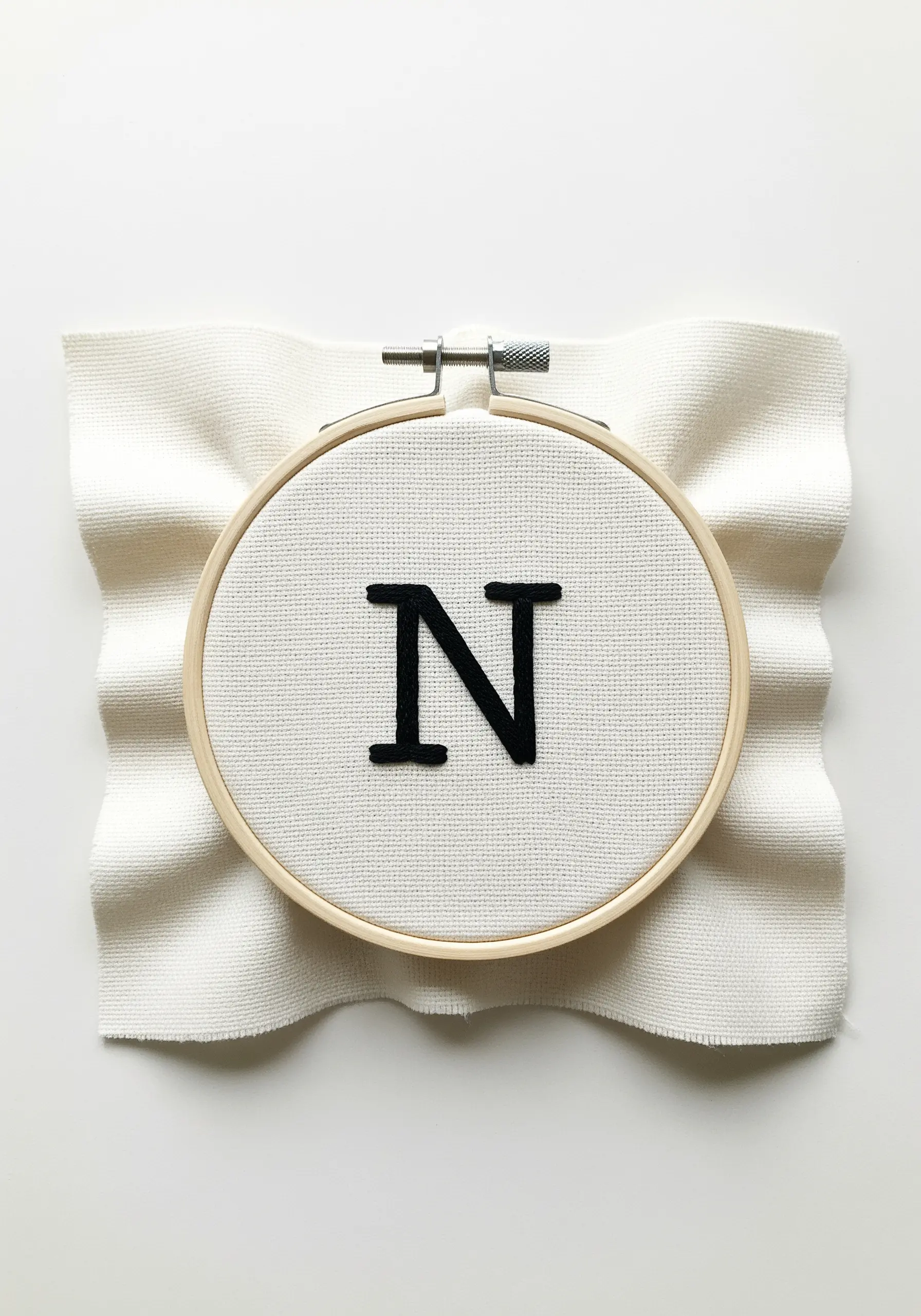 A single black serif 'N' in satin stitch on off-white Aida cloth.