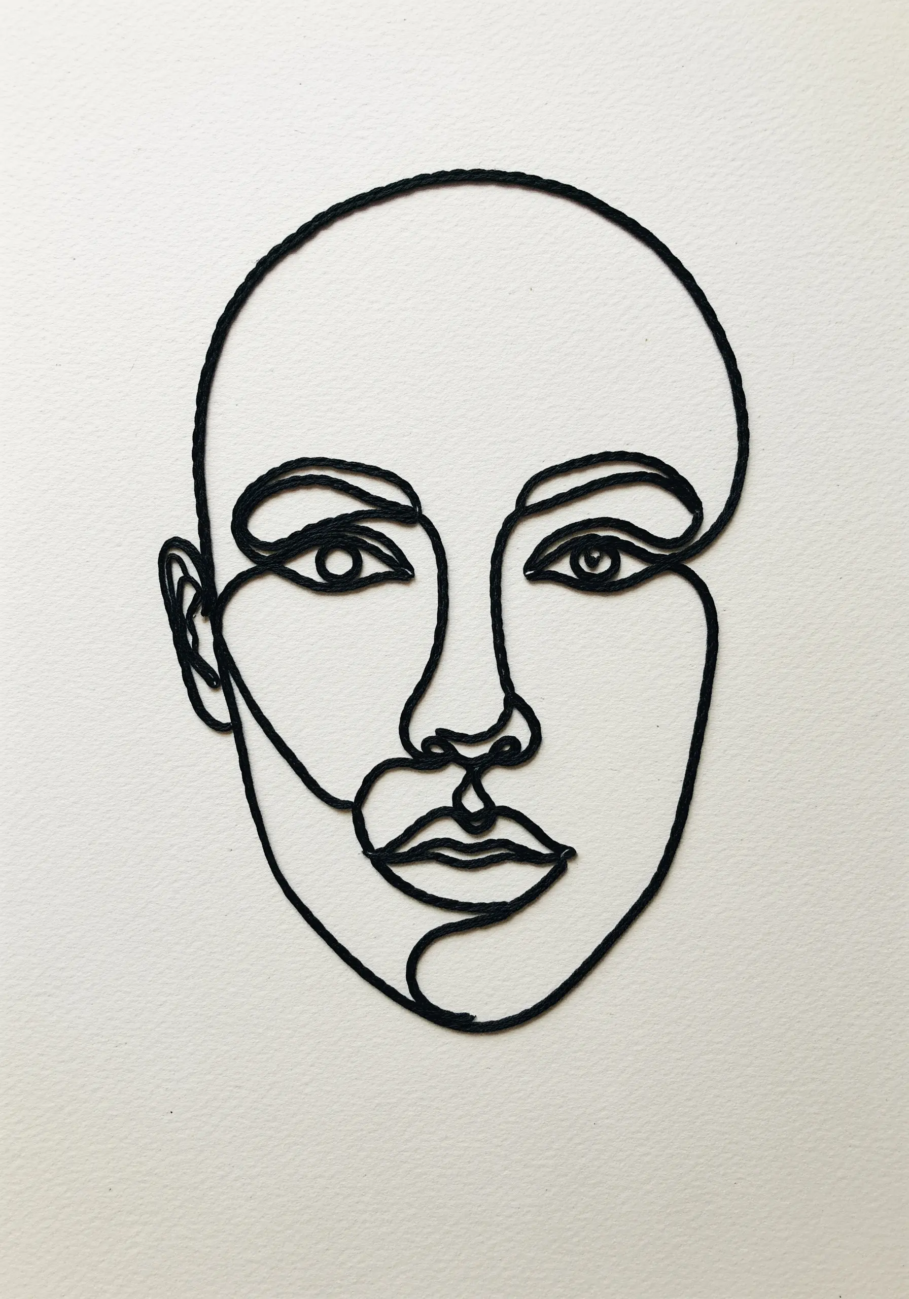 A minimalist portrait created from a single piece of black cord arranged on a white background.