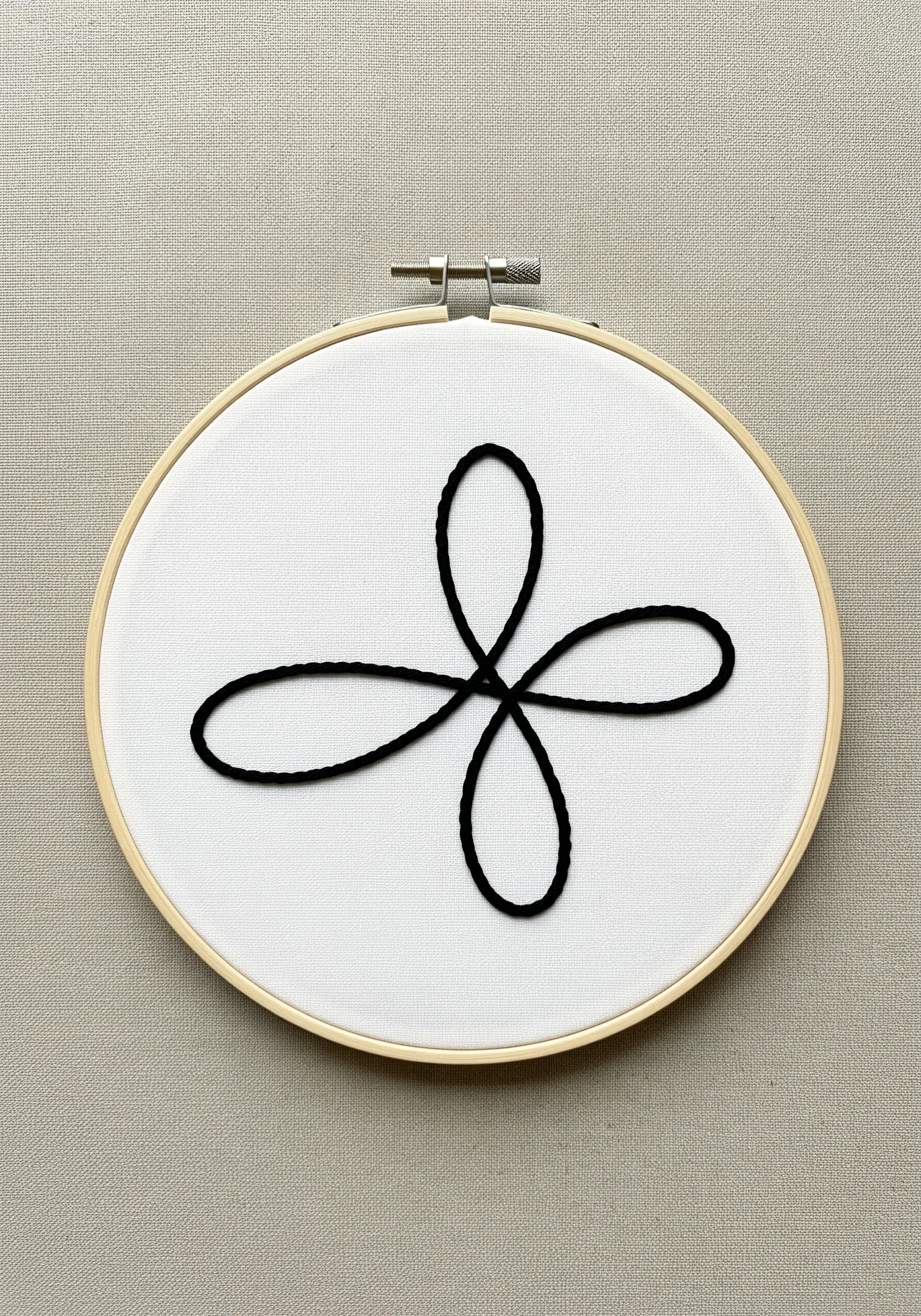 A single continuous black looped line couched onto white fabric in a hoop.