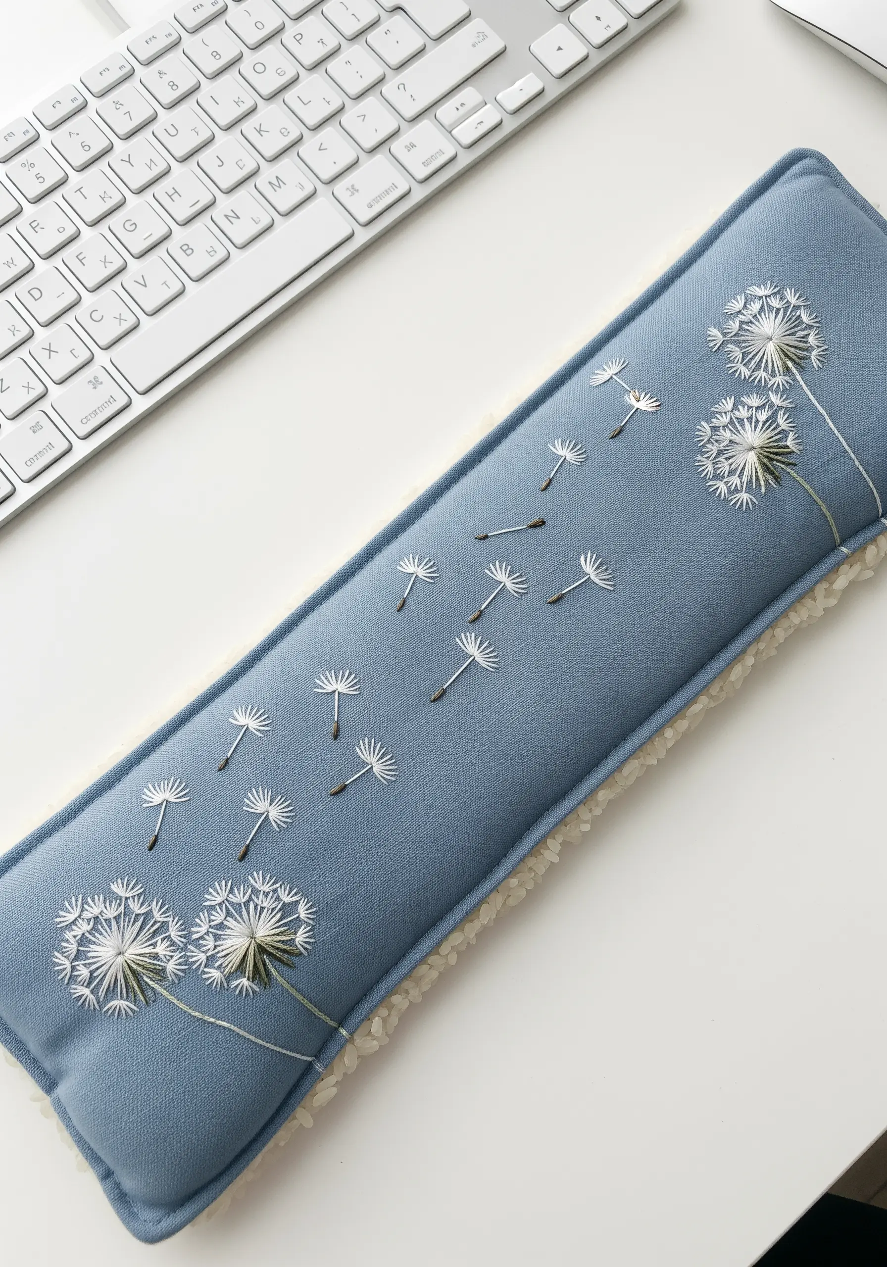 A blue keyboard wrist rest embroidered with delicate white dandelion seeds.