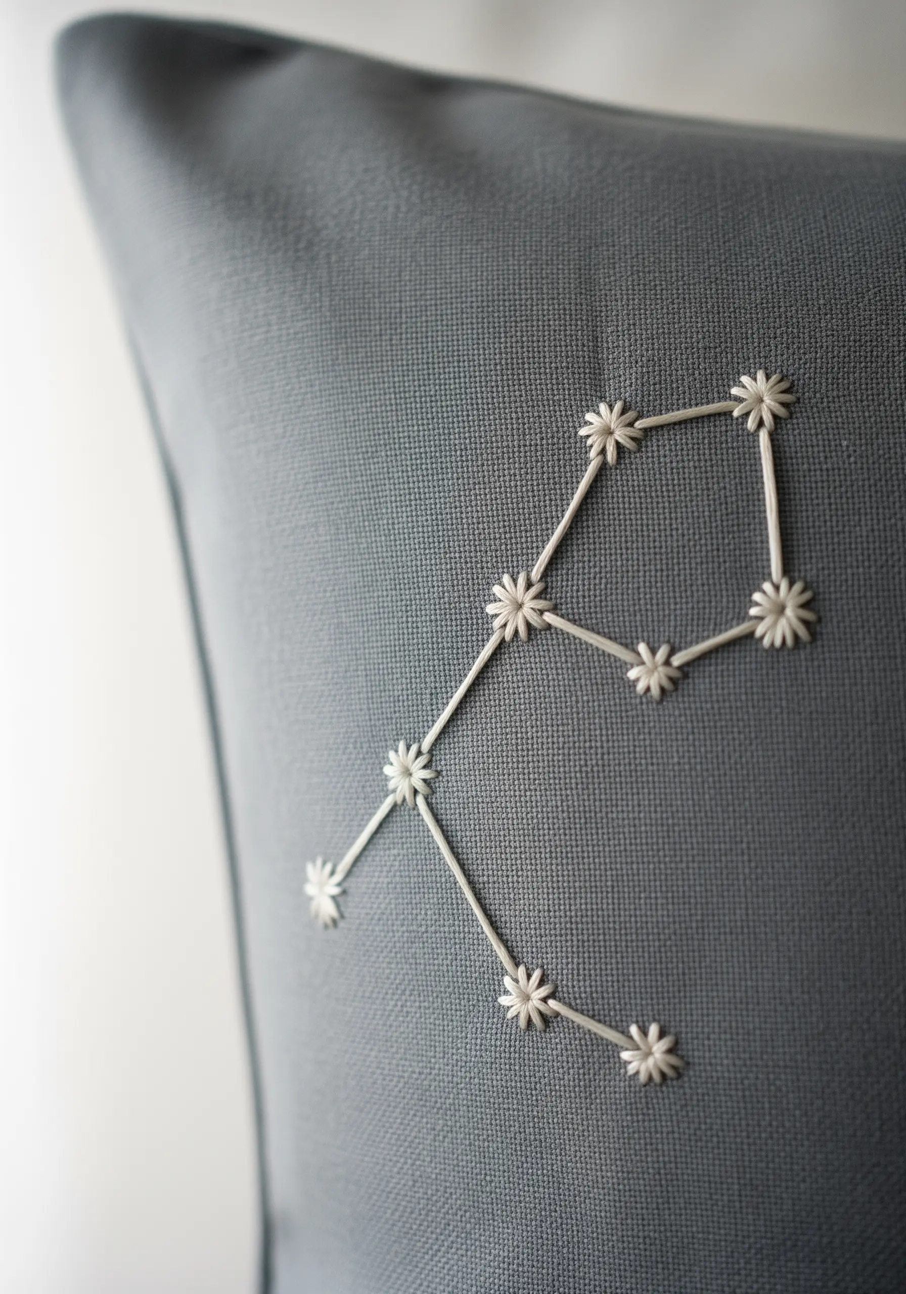 A constellation embroidered in white thread on a dark gray pillowcase, with star-shaped stitches.
