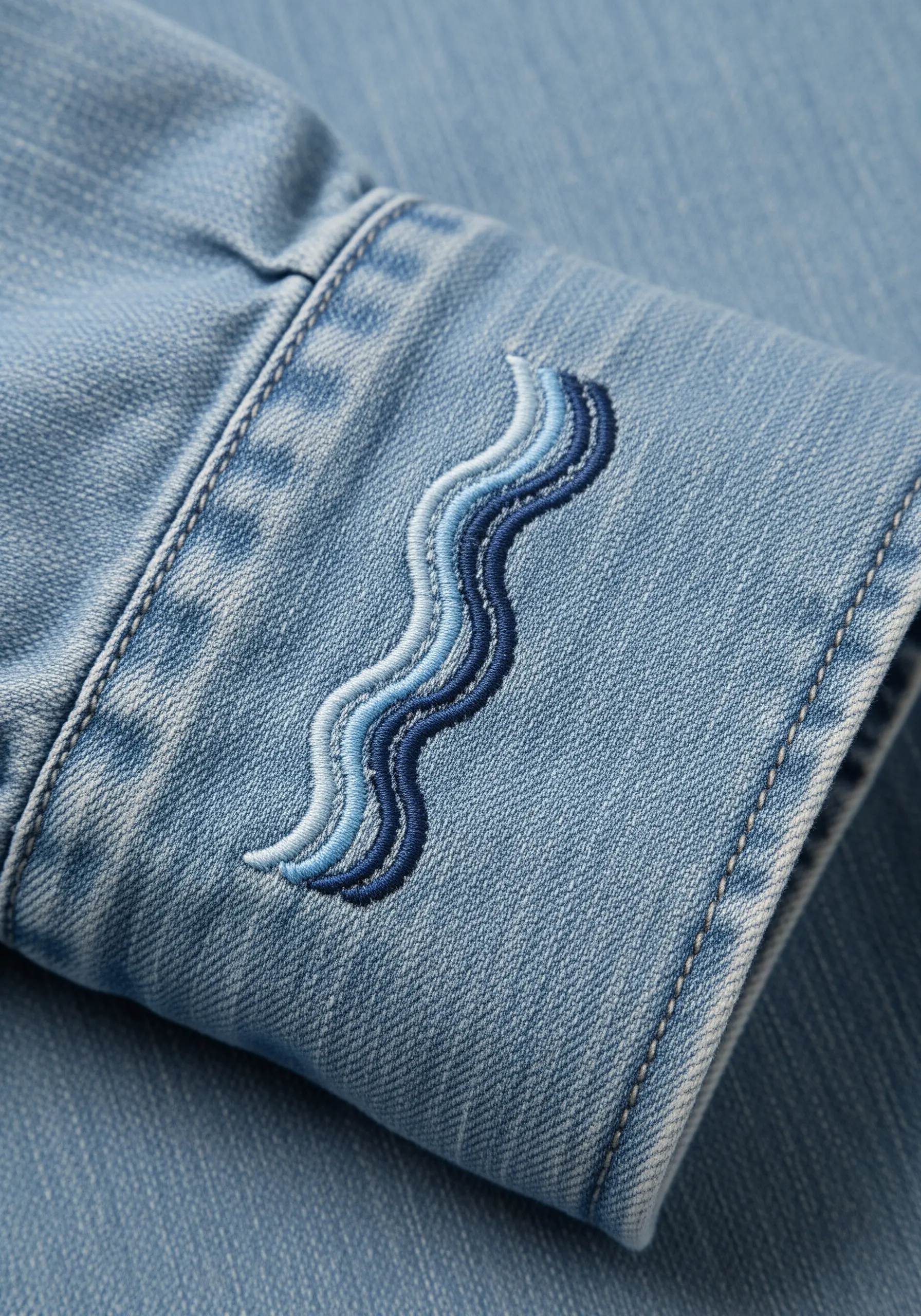 Abstract wave motif embroidered on a denim cuff using four shades of blue thread.