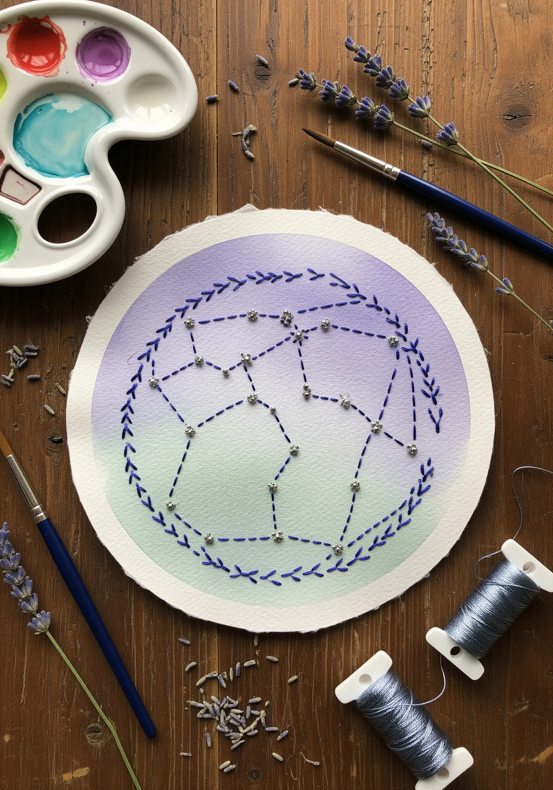 A constellation embroidered on paper with a purple and green watercolor background.