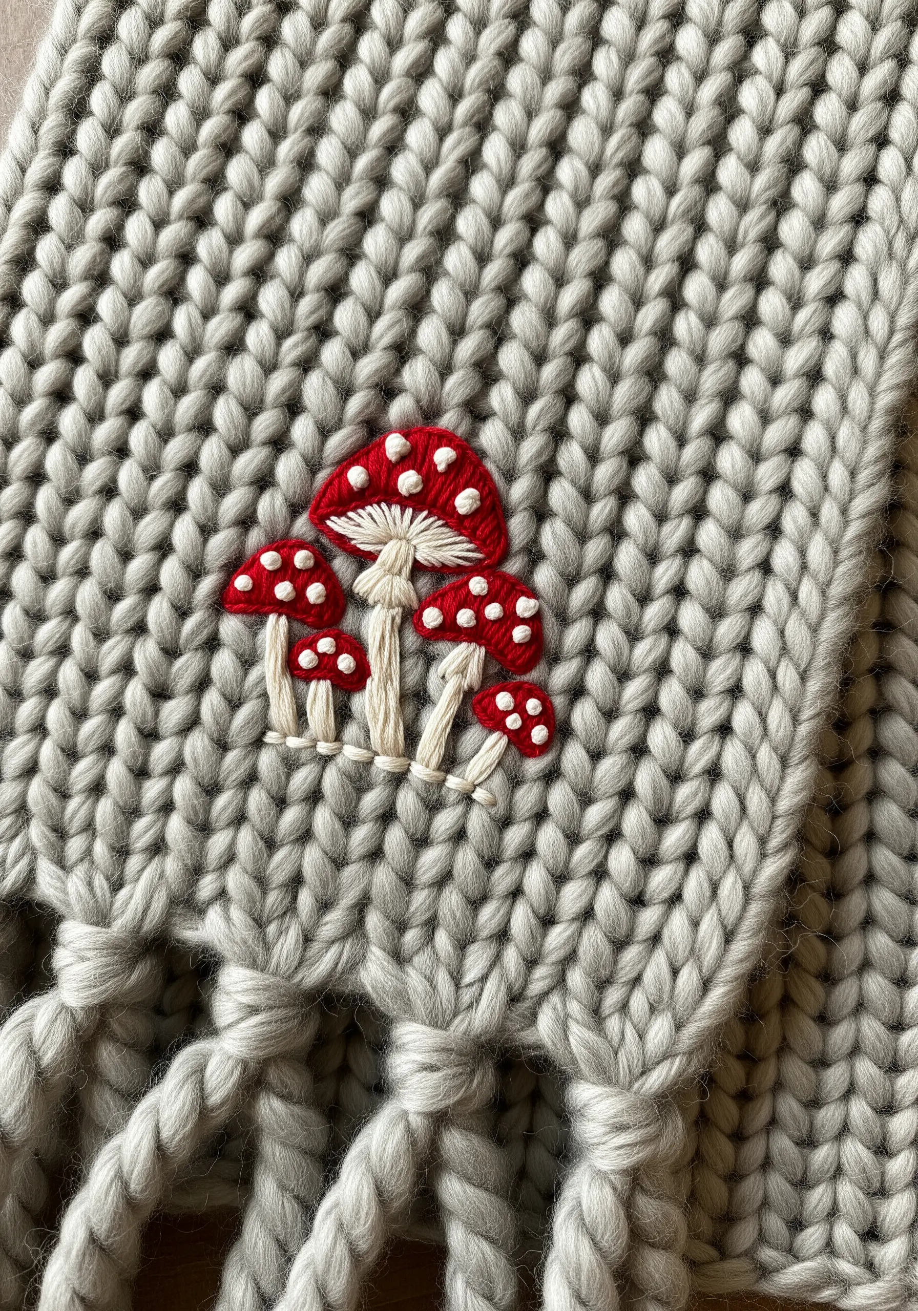 A cluster of red and white fly agaric mushrooms embroidered on a chunky gray knit scarf.