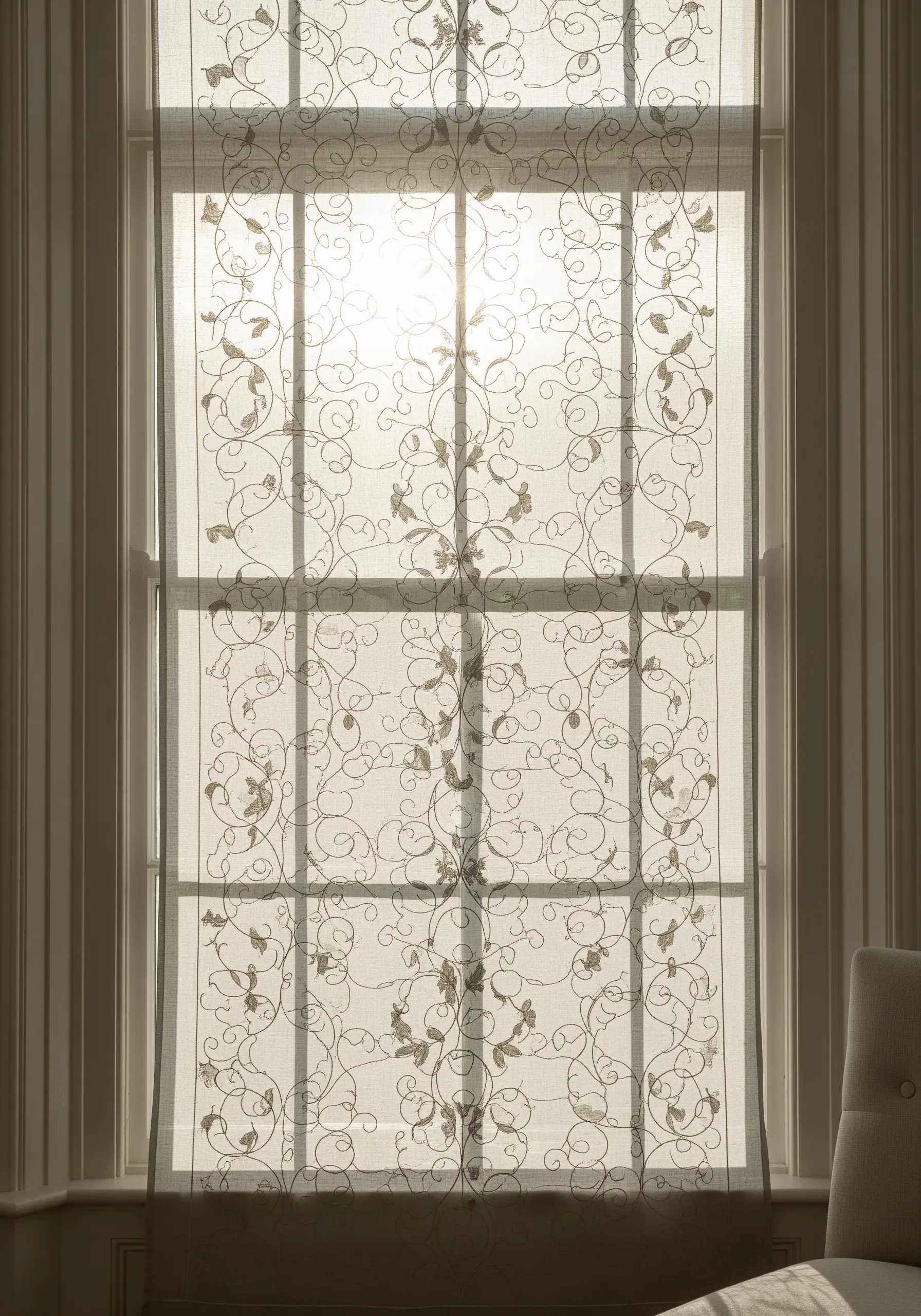 Sheer window curtains with a delicate, swirling vine pattern embroidered in a light metallic thread.
