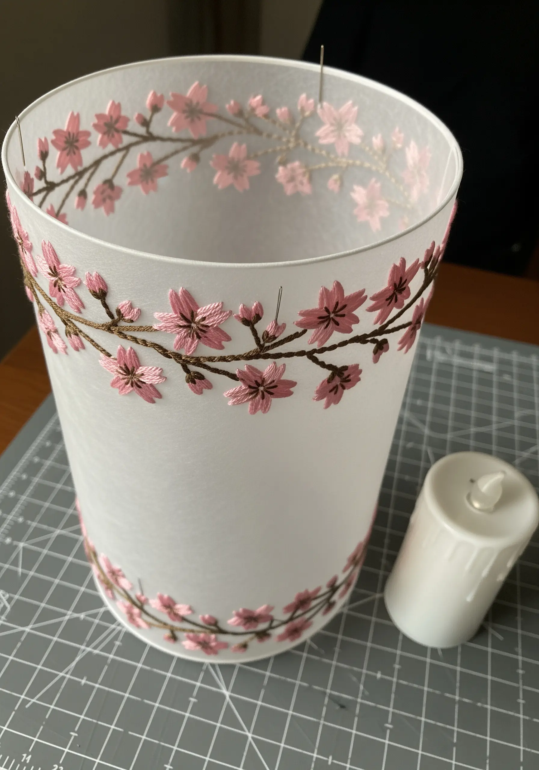 A paper lantern sleeve embroidered with pink cherry blossoms, shown with an LED candle.