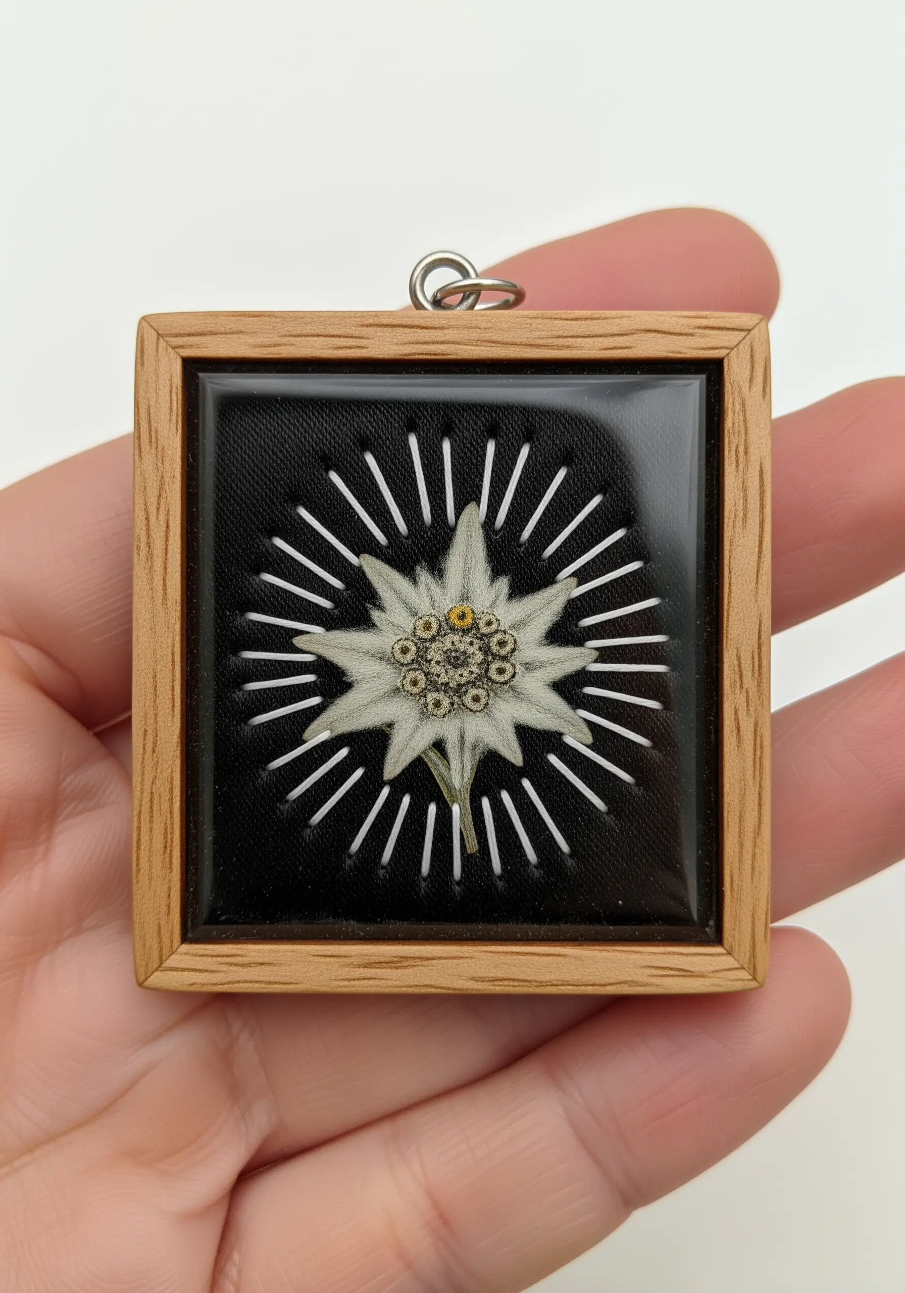 A pressed edelweiss flower with radiating white stitches, encased in resin in a small wooden frame.