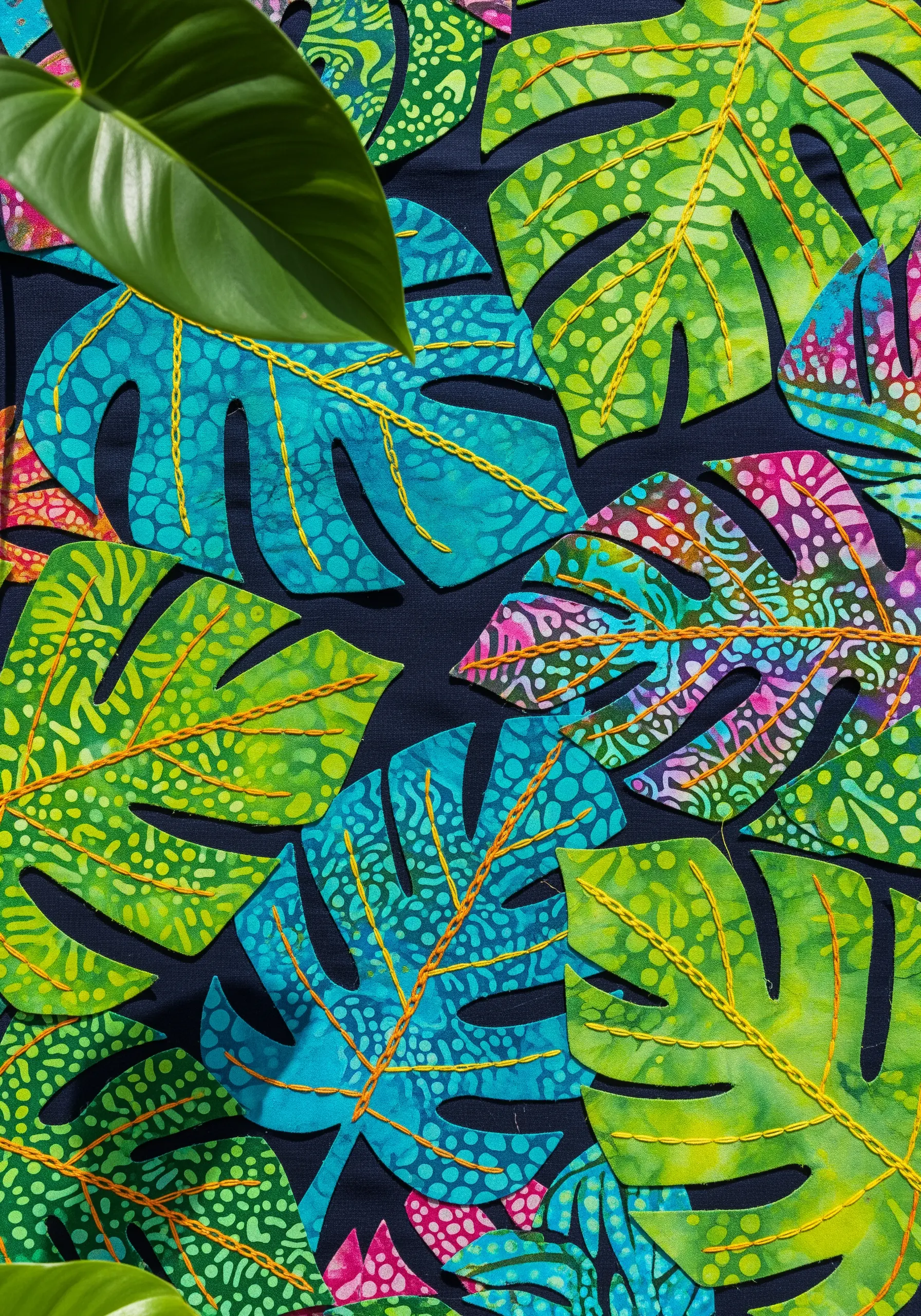 Vibrant, patterned fabric leaves appliquéd onto a dark background, with yellow running stitches for veins.
