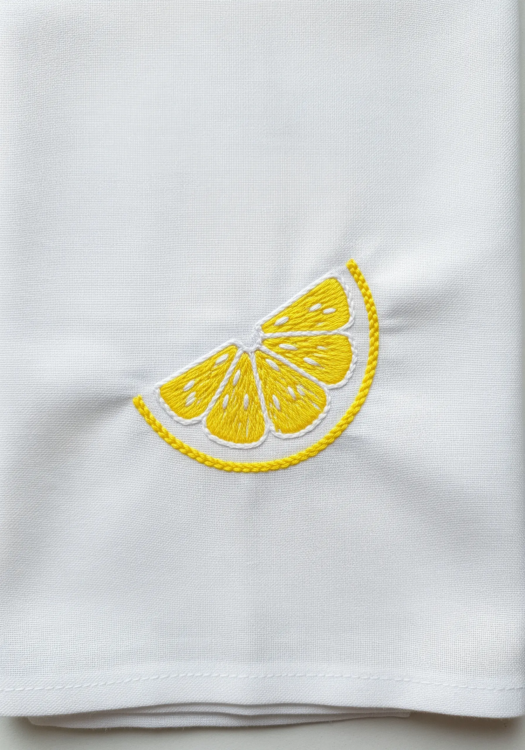 An embroidered lemon slice with a bright yellow chain stitch outline on white fabric.