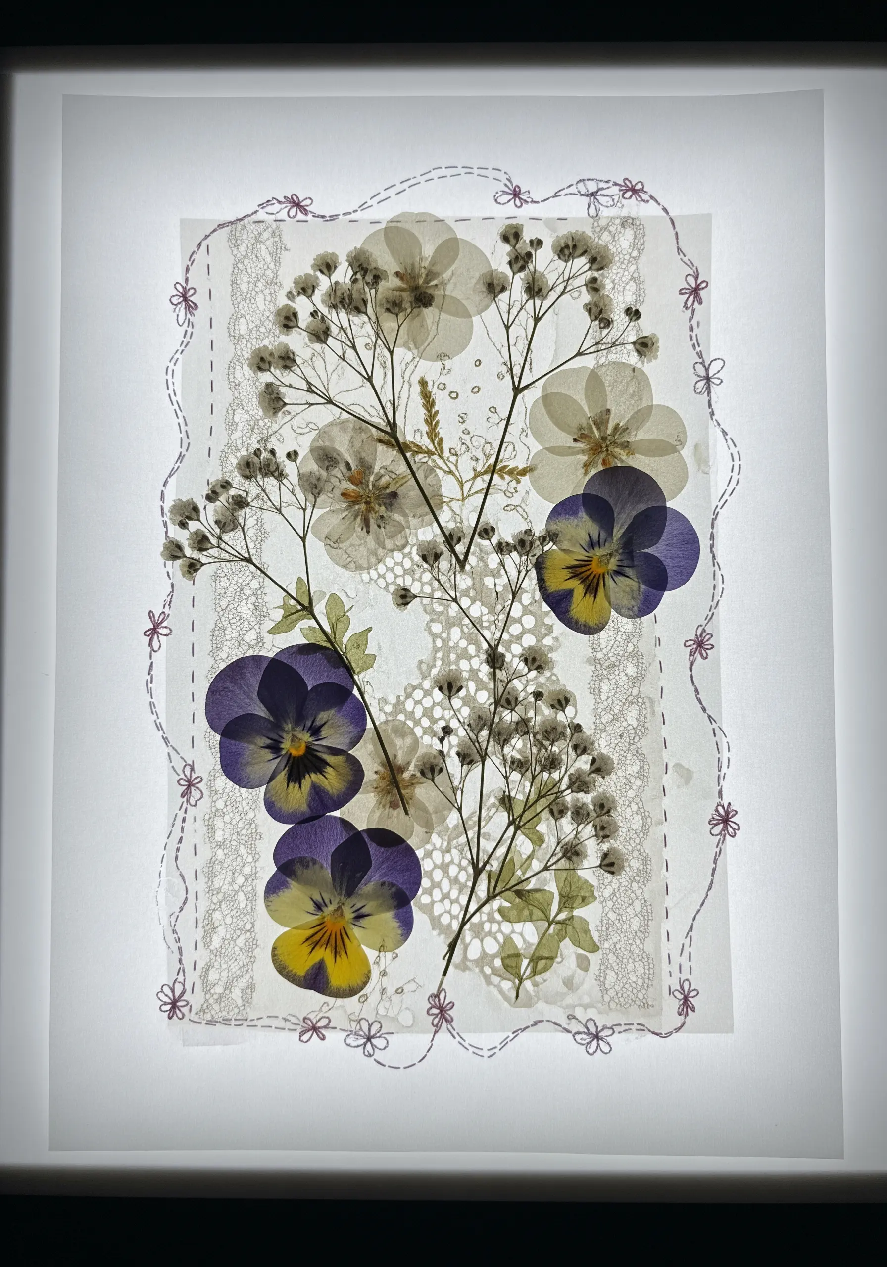 Pressed pansies and baby's breath on lace paper, framed with delicate embroidery.