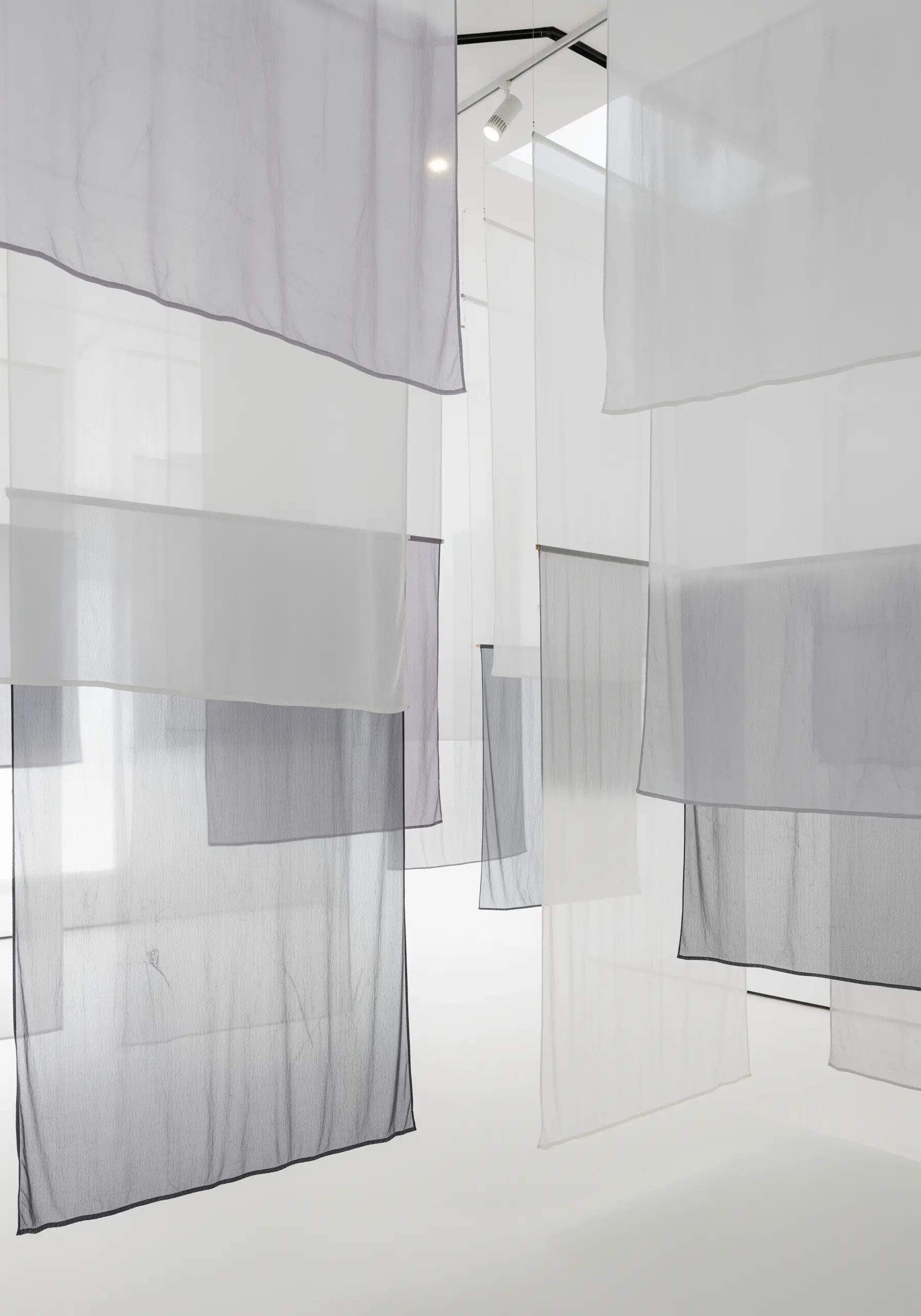 An installation of sheer white and gray fabric panels hanging in layers.