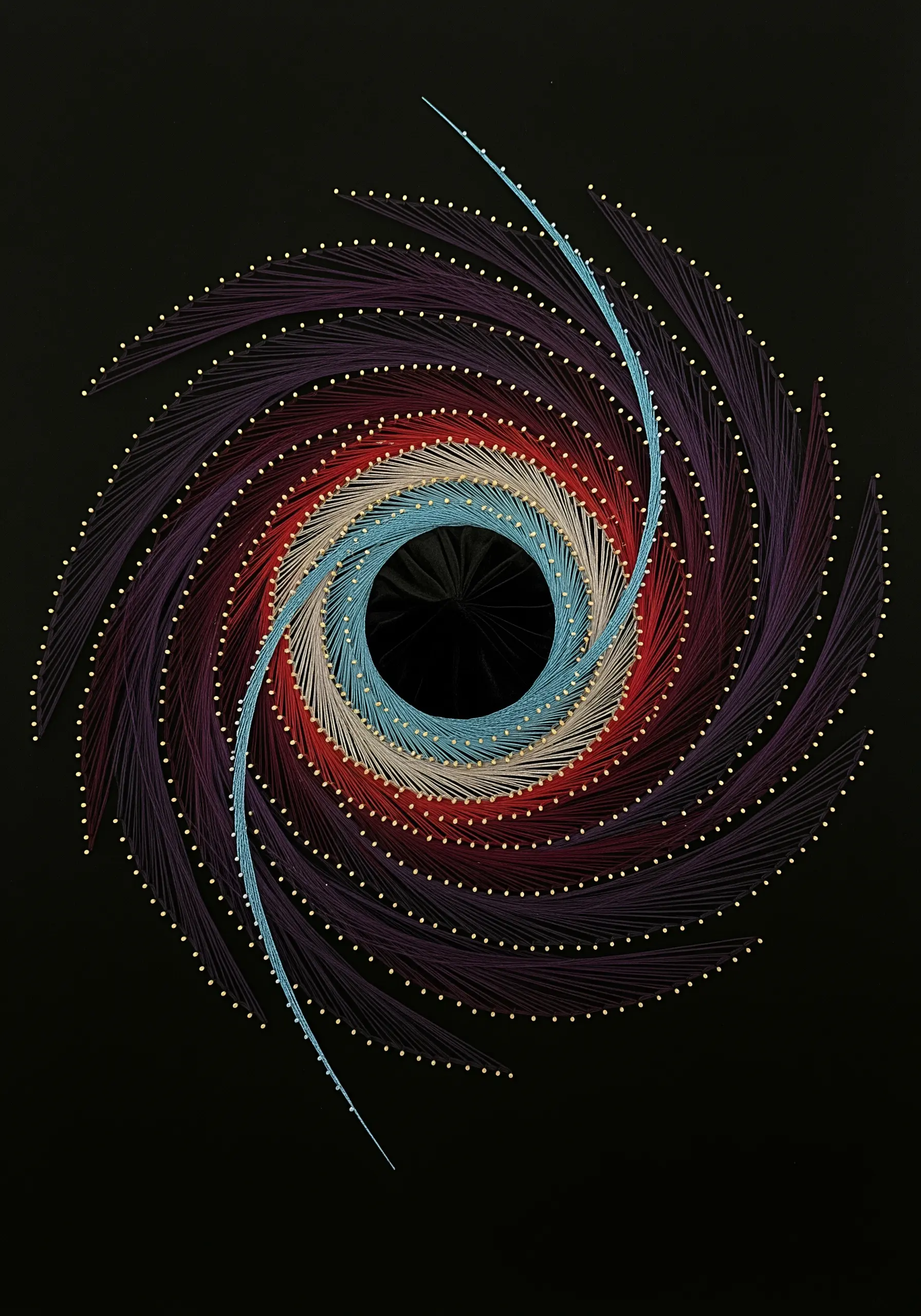 Spiral string art with a dark center, radiating outwards with blue, red, and purple threads.