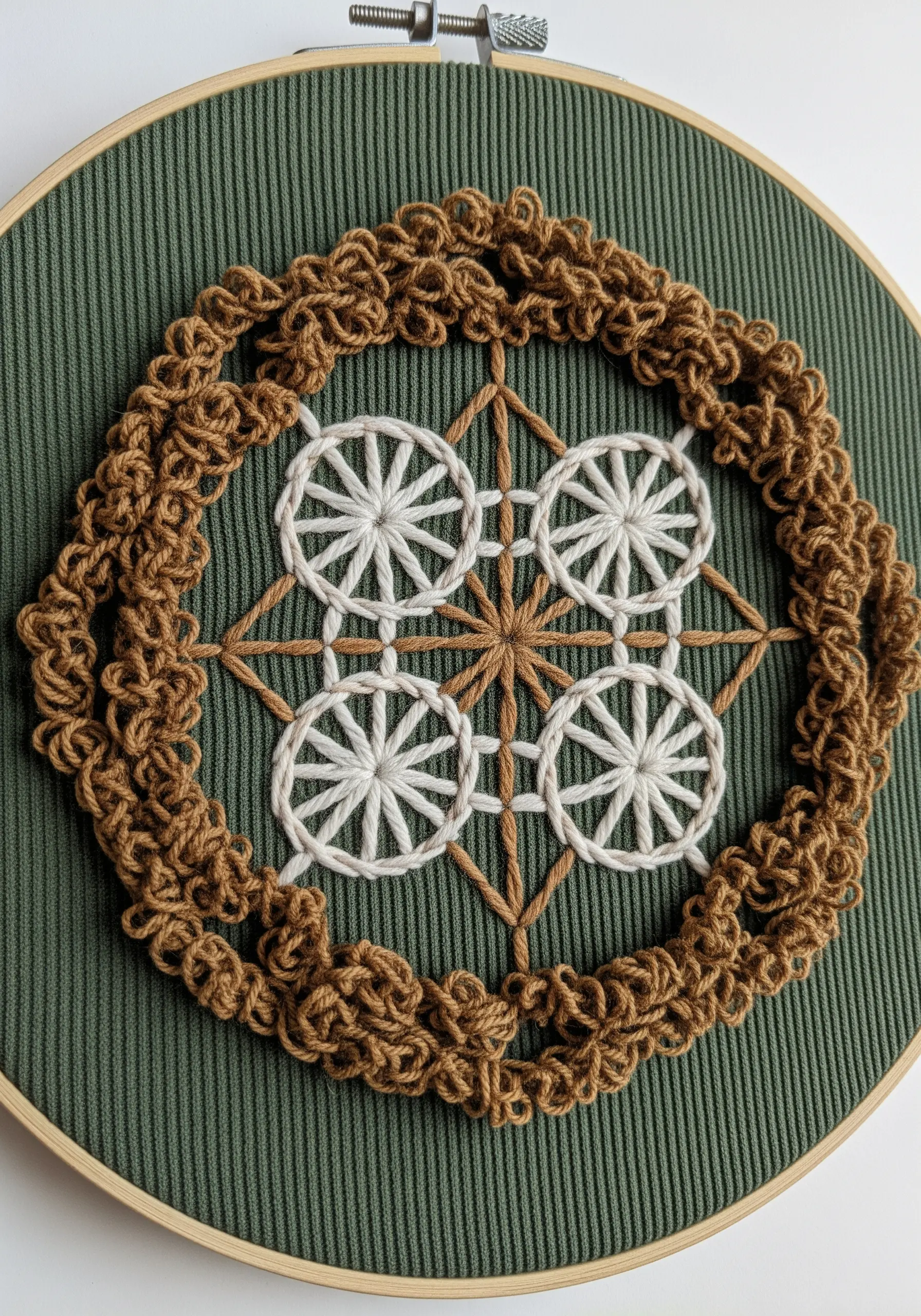 Mandala with a highly textured bullion knot border and woven spider wheels on green corduroy fabric.