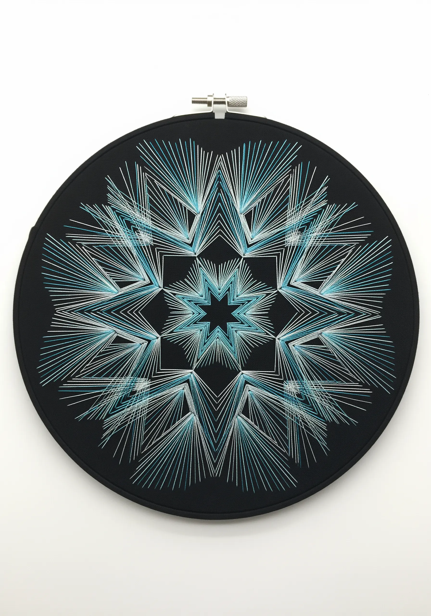 Geometric string art mandala with blue and white threads creating layered star shapes on black fabric.