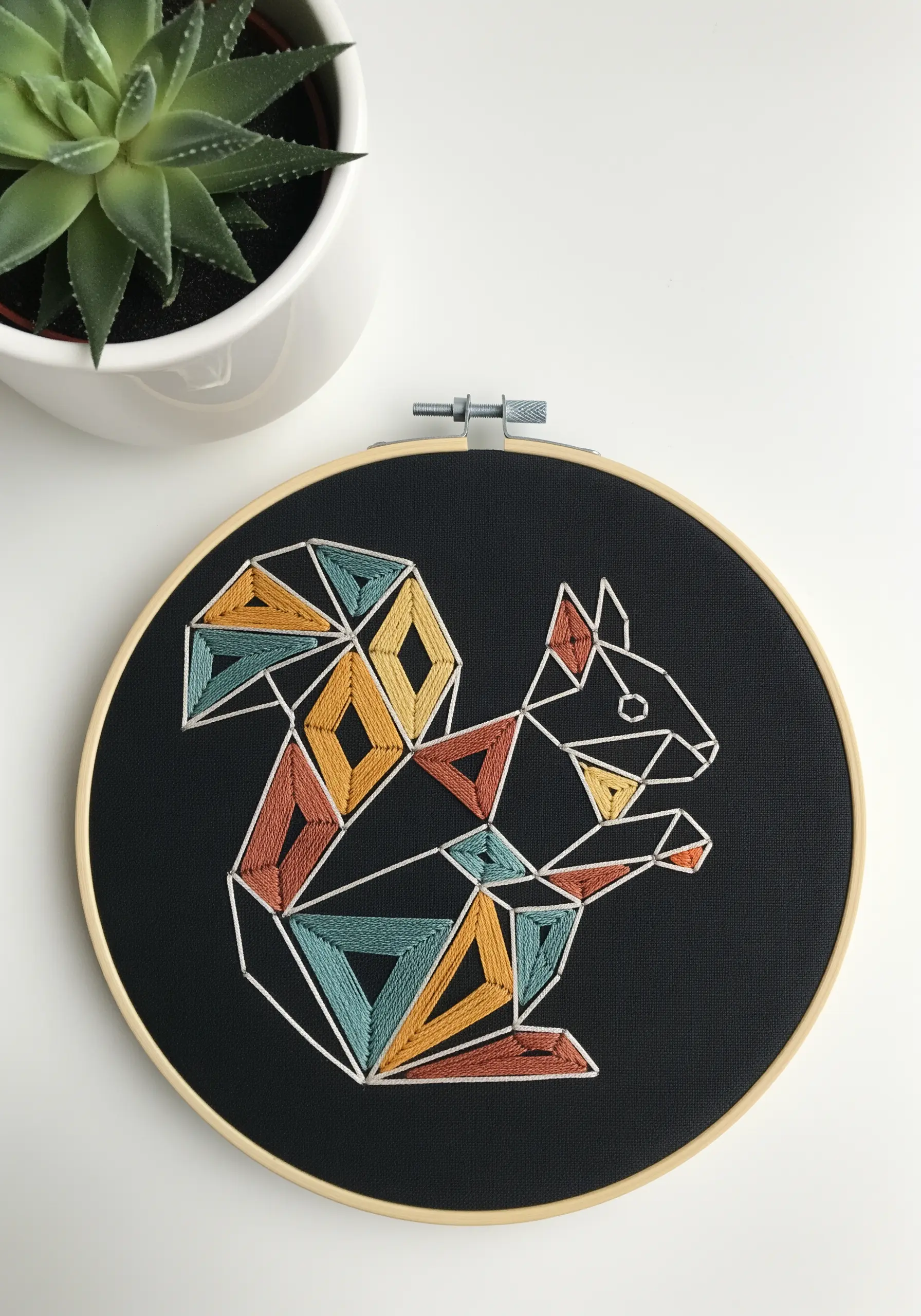 Modern geometric embroidery of a squirrel on black fabric with colorful shapes.