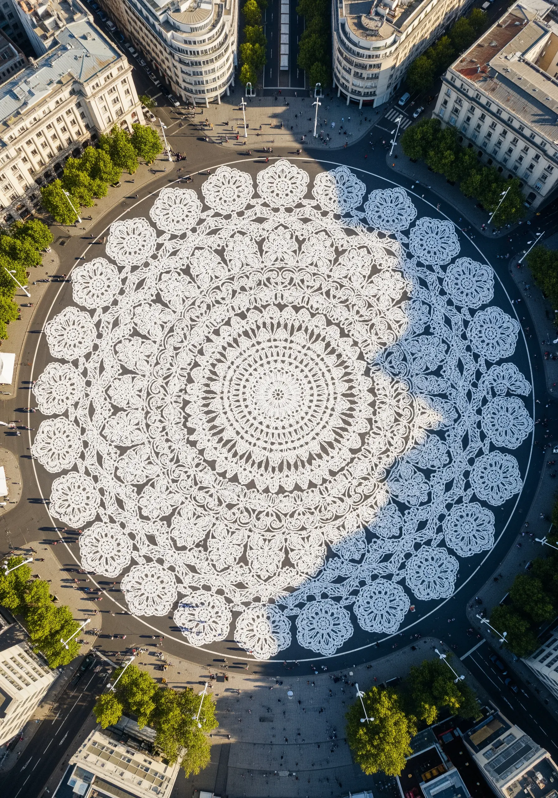 An aerial view of a massive, white lace doily pattern installed in a city roundabout.