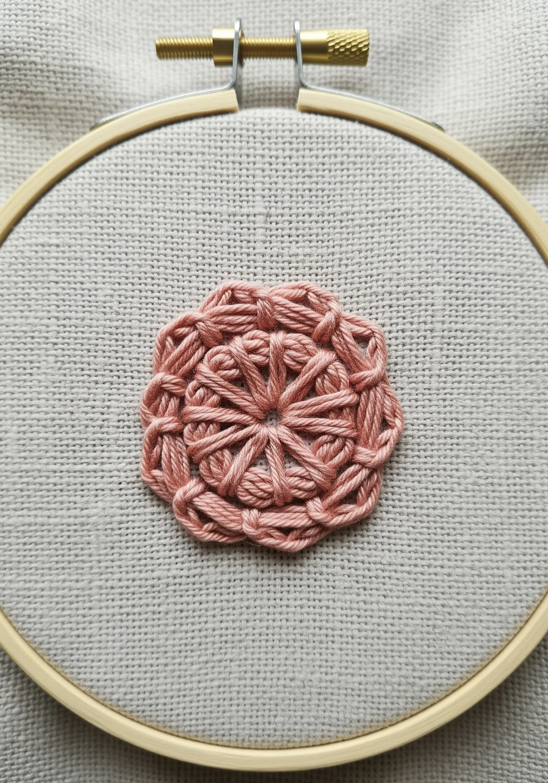 A pink woven wheel stitch creating a raised, textured circular floral motif.
