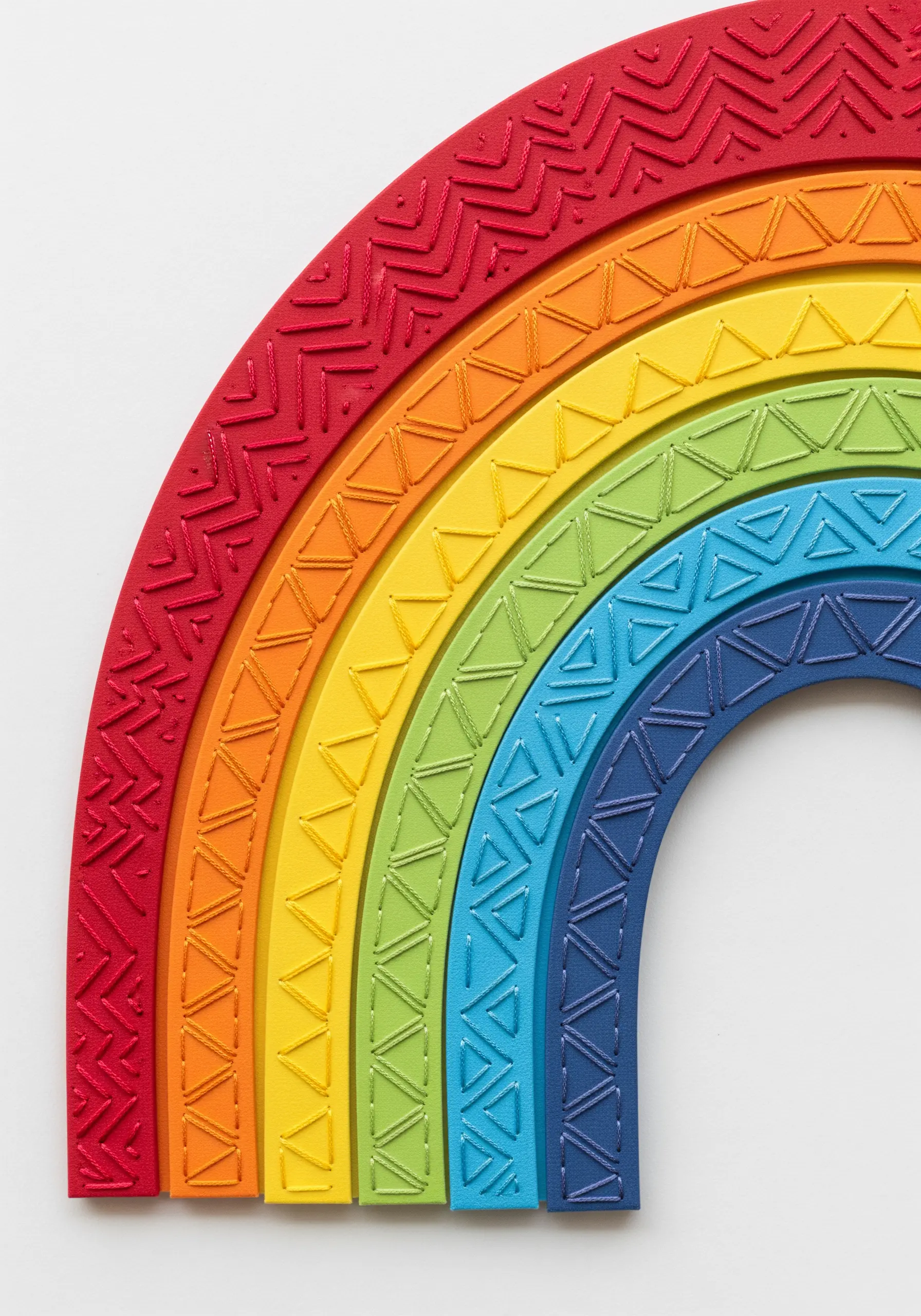 A close-up of a rainbow wall art piece, where each colored arch has a unique stitched texture.