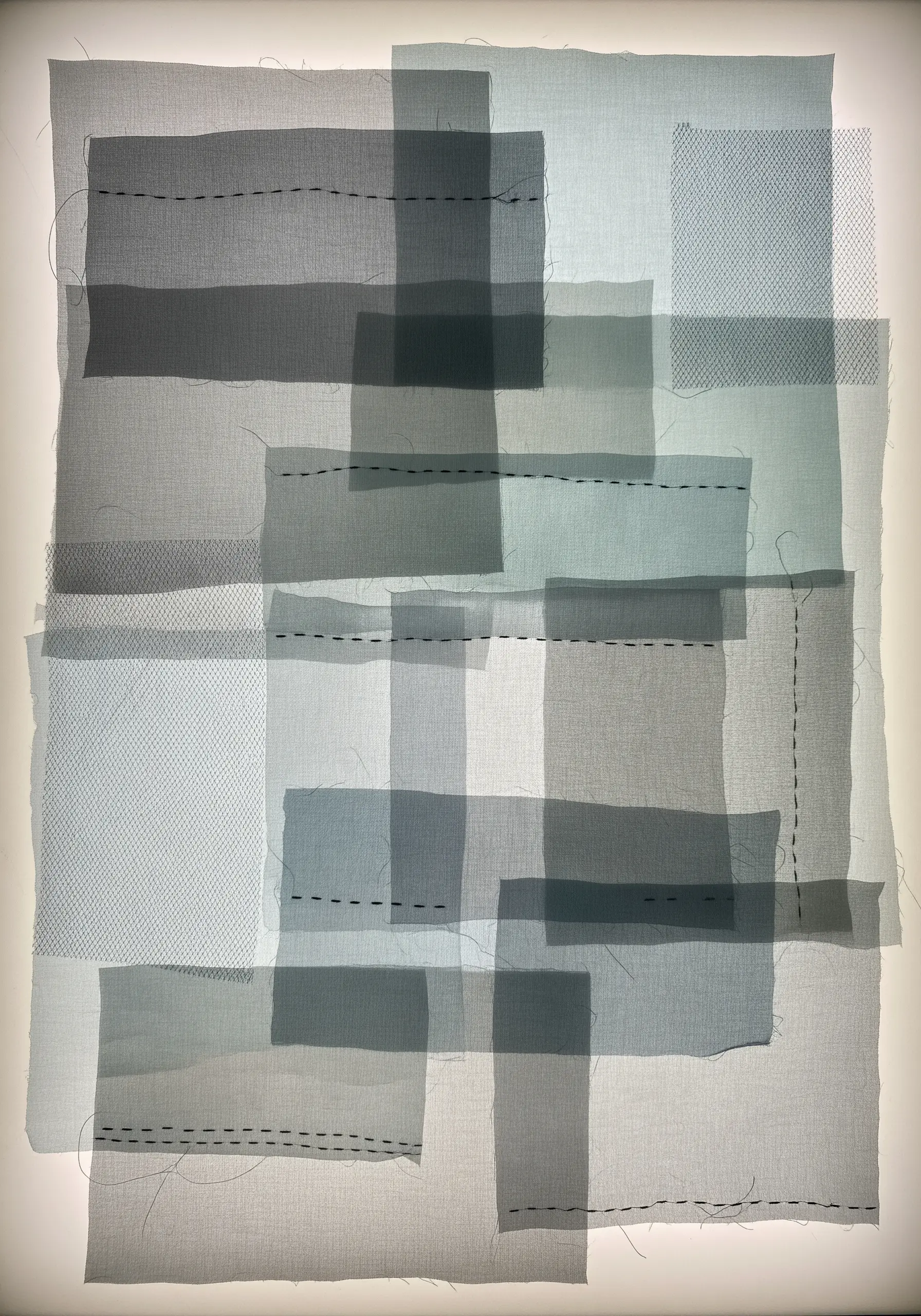 A backlit collage of layered sheer grey fabrics, revealing different levels of transparency and texture.