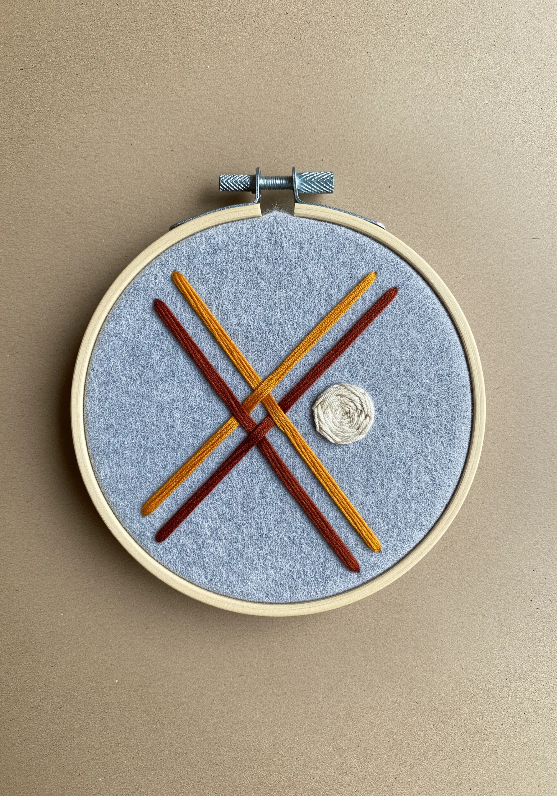 Abstract design with woven threads and a woven wheel stitch on gray felt.