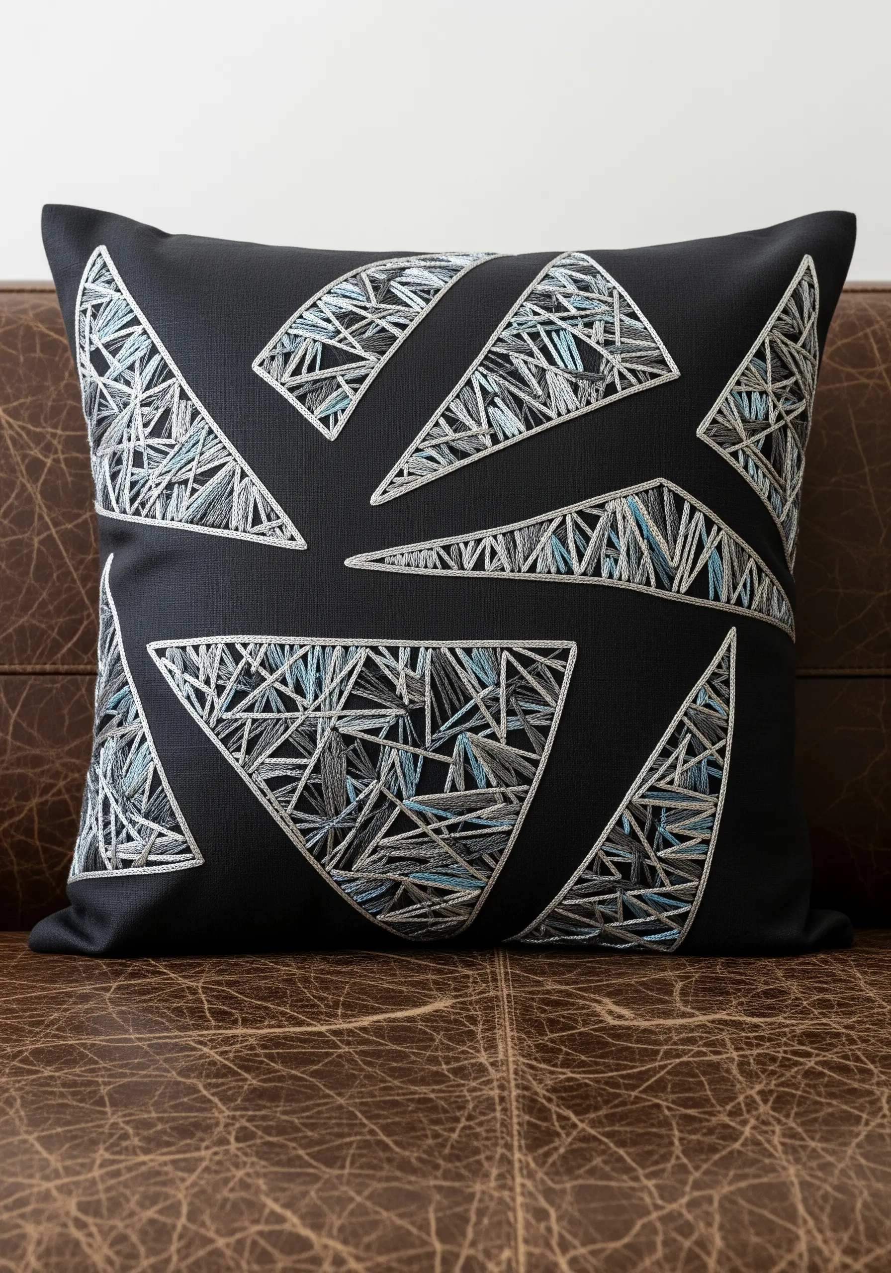 A black pillow with triangles outlined in white and filled with chaotic, multi-colored stitches.