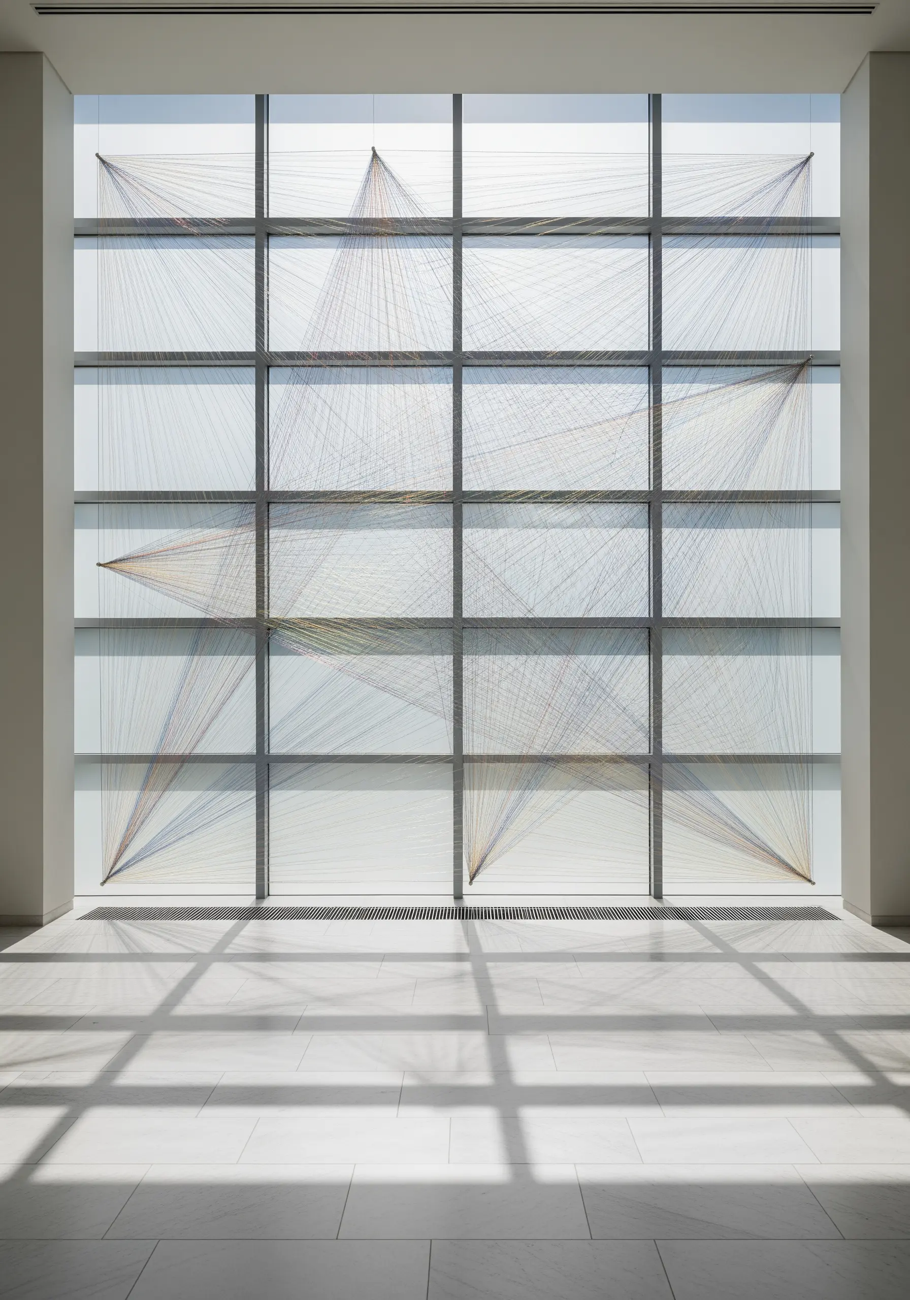 Colorful threads stretched across a large window grid, creating a stained-glass effect.