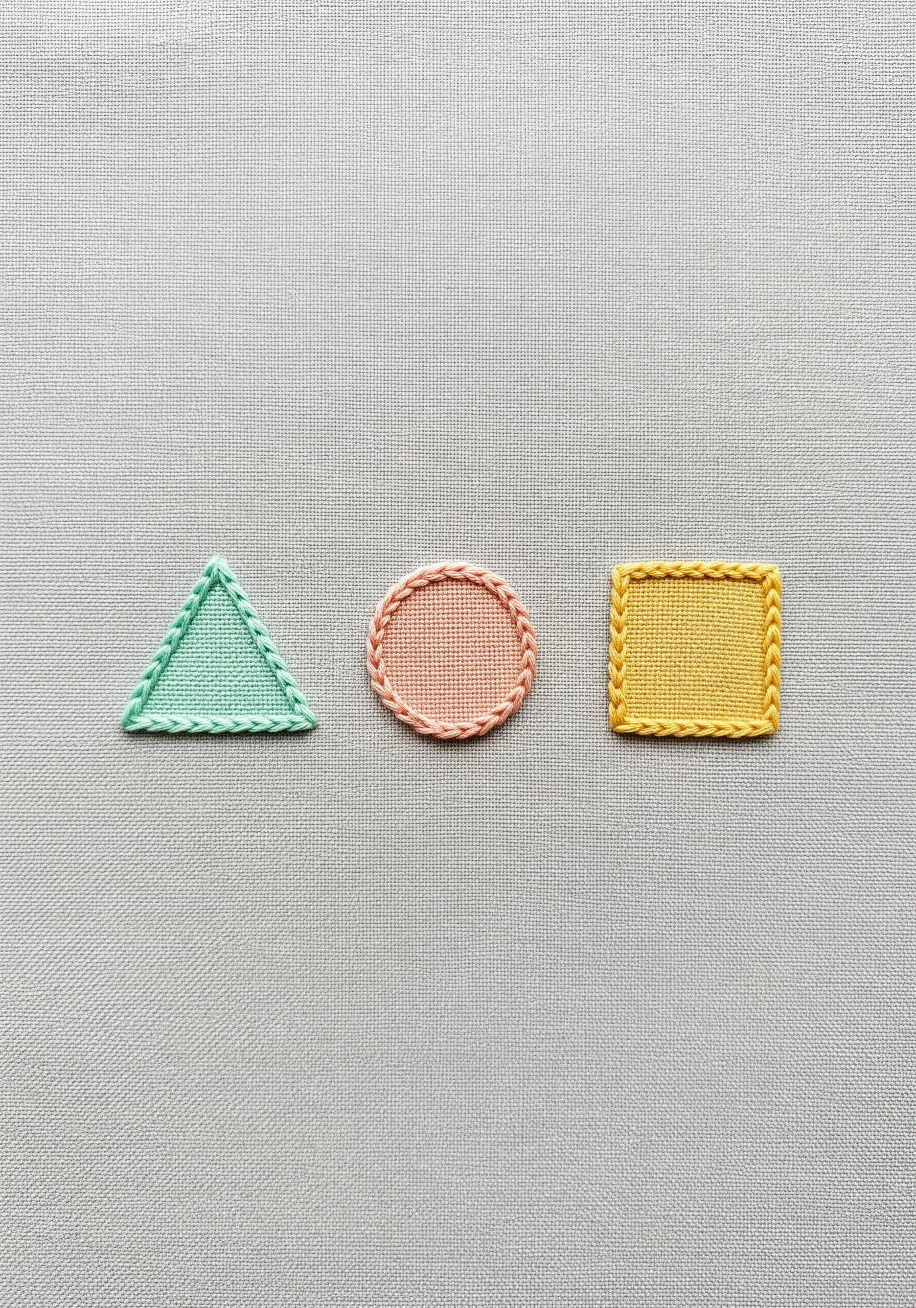 Three small embroidered patches—a triangle, circle, and square—with neatly whipped edges.