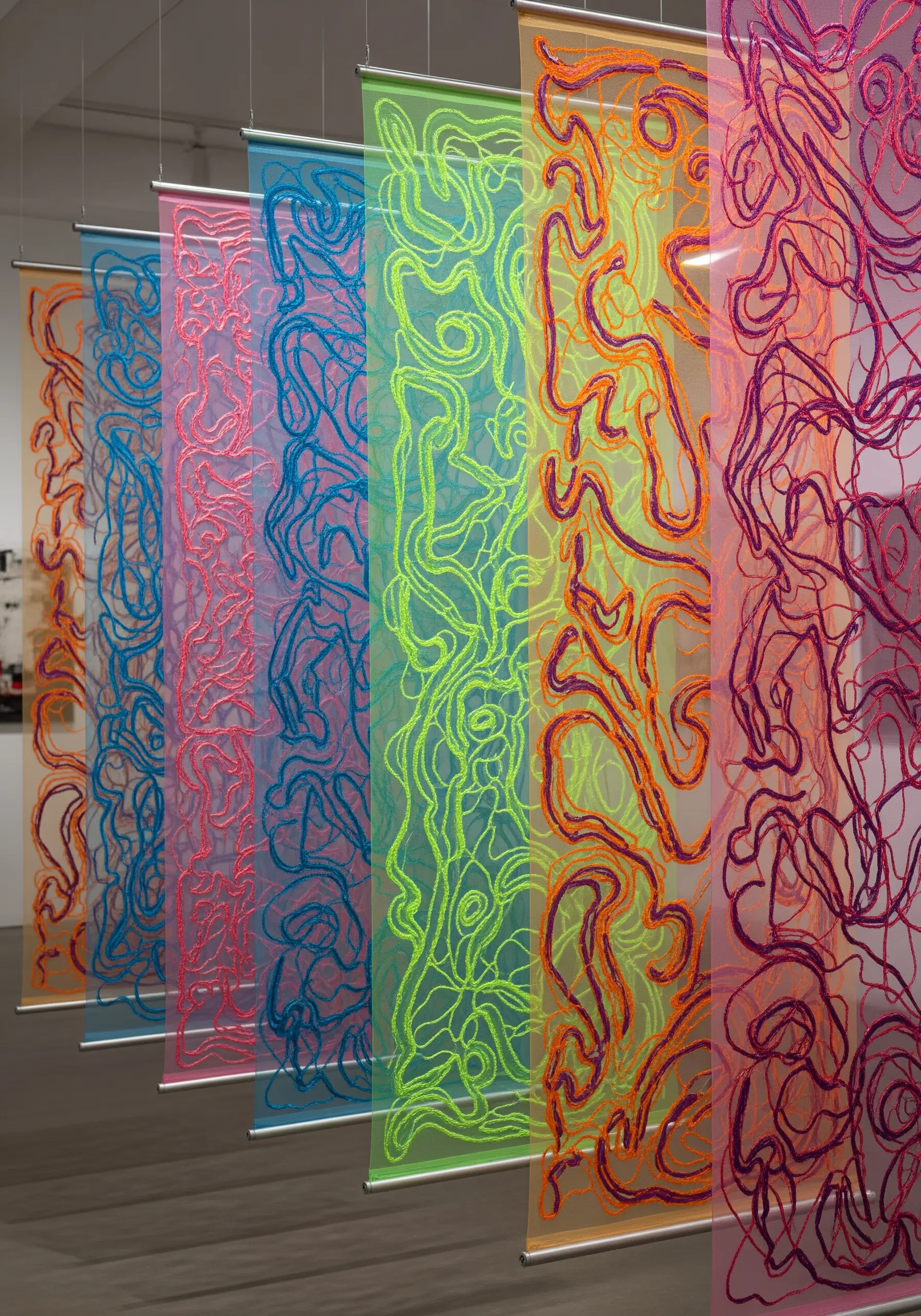 Colorful abstract line embroidery on sheer, transparent panels hanging in a gallery space