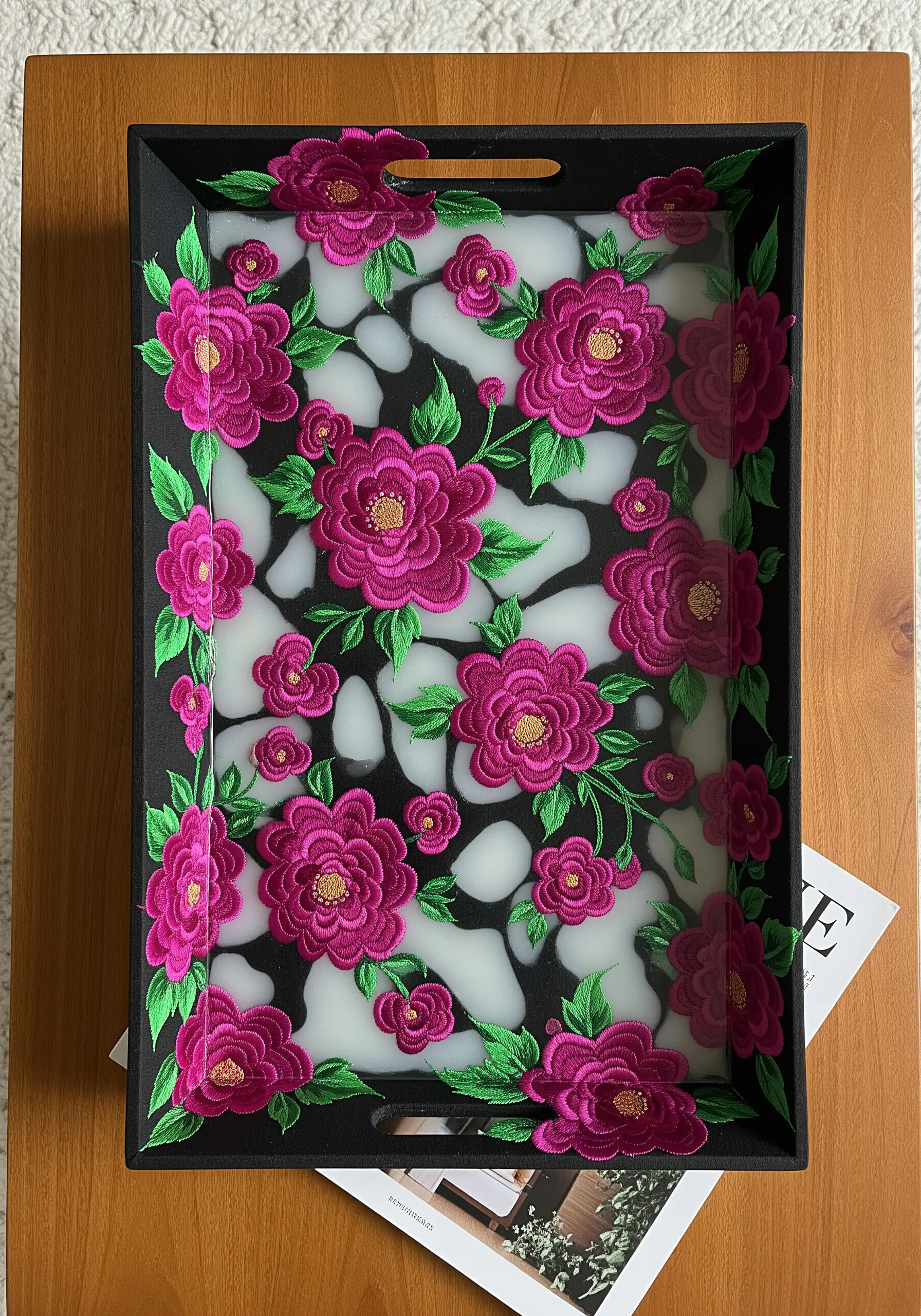 Embroidered magenta flowers set in milky white resin on a black serving tray.