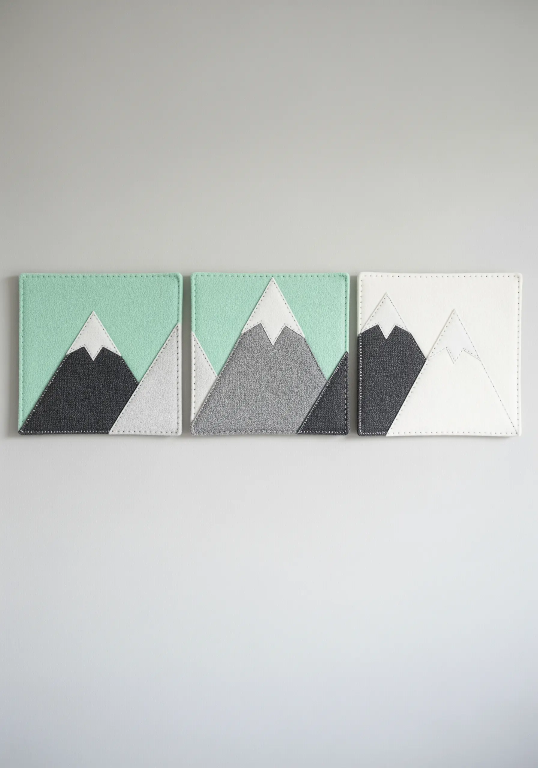 A set of three minimalist textile art squares depicting a modern mountain range.