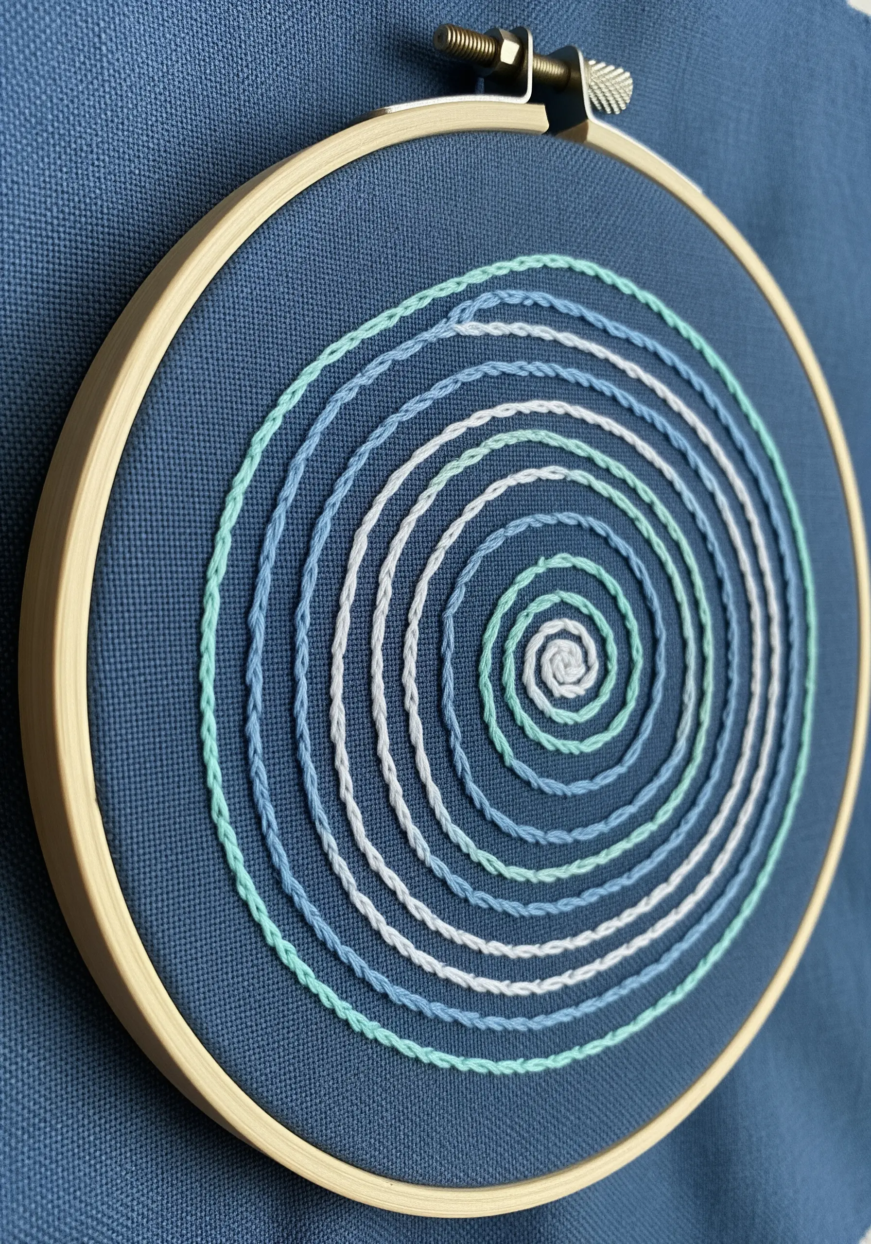 A spiral of whipped backstitch in shades of blue and white on a dark blue fabric.