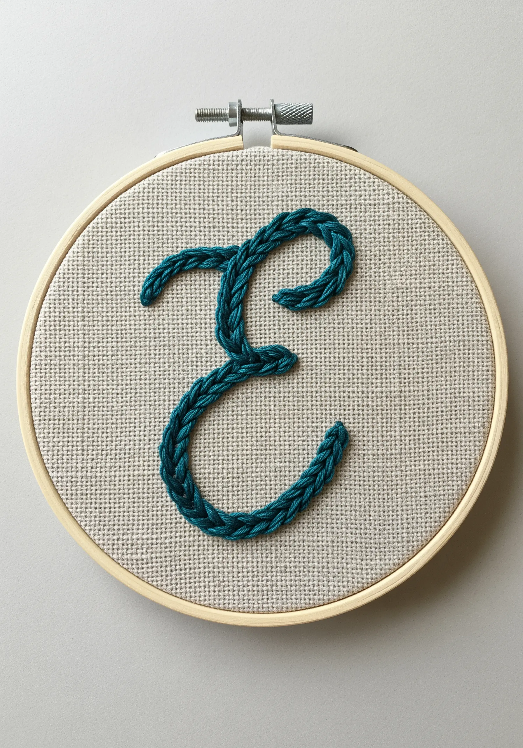 A cursive 'E' in a thick, braided teal chain stitch.