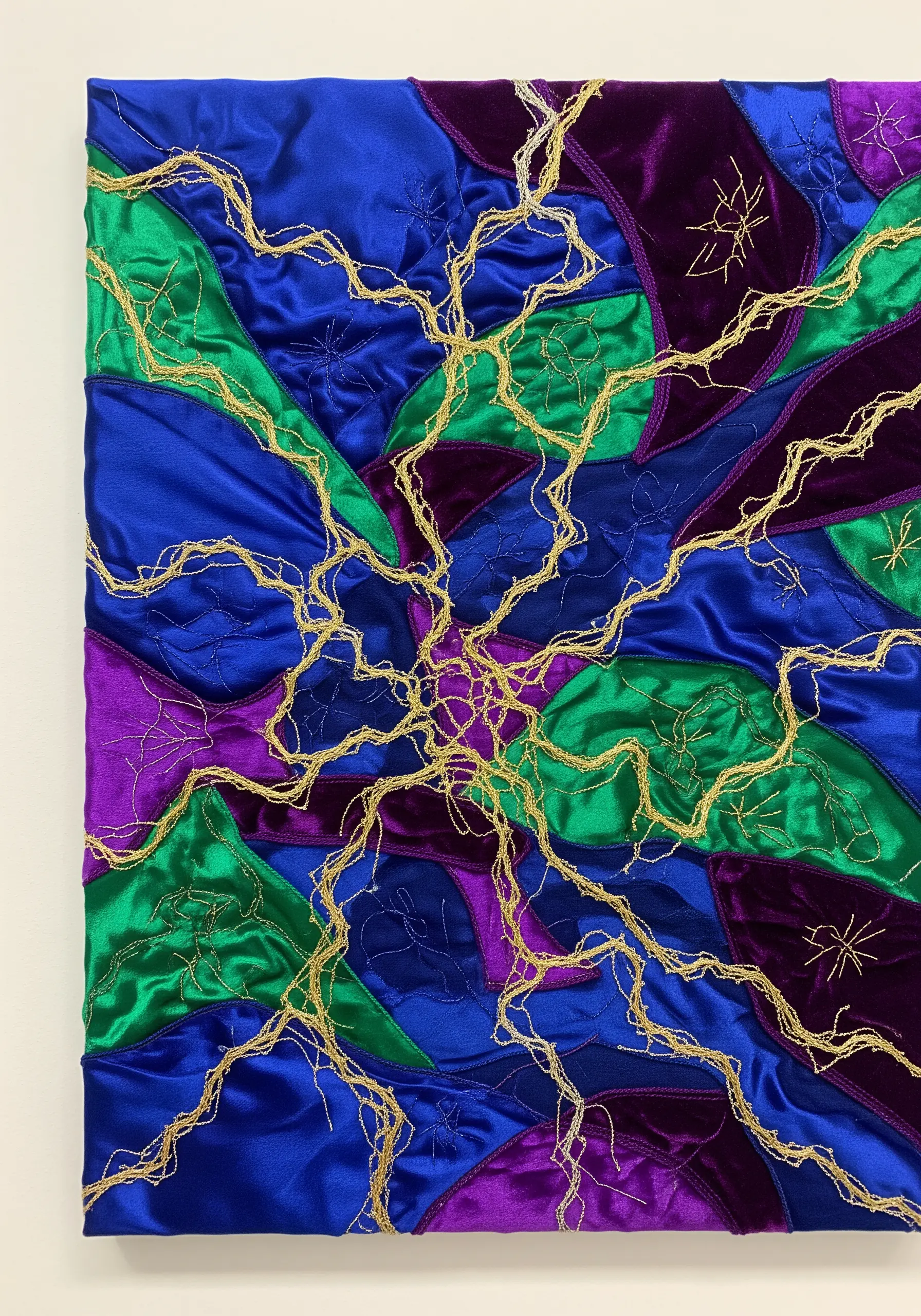 Abstract collage of blue, purple, and green satin with energetic gold thread embroidery.