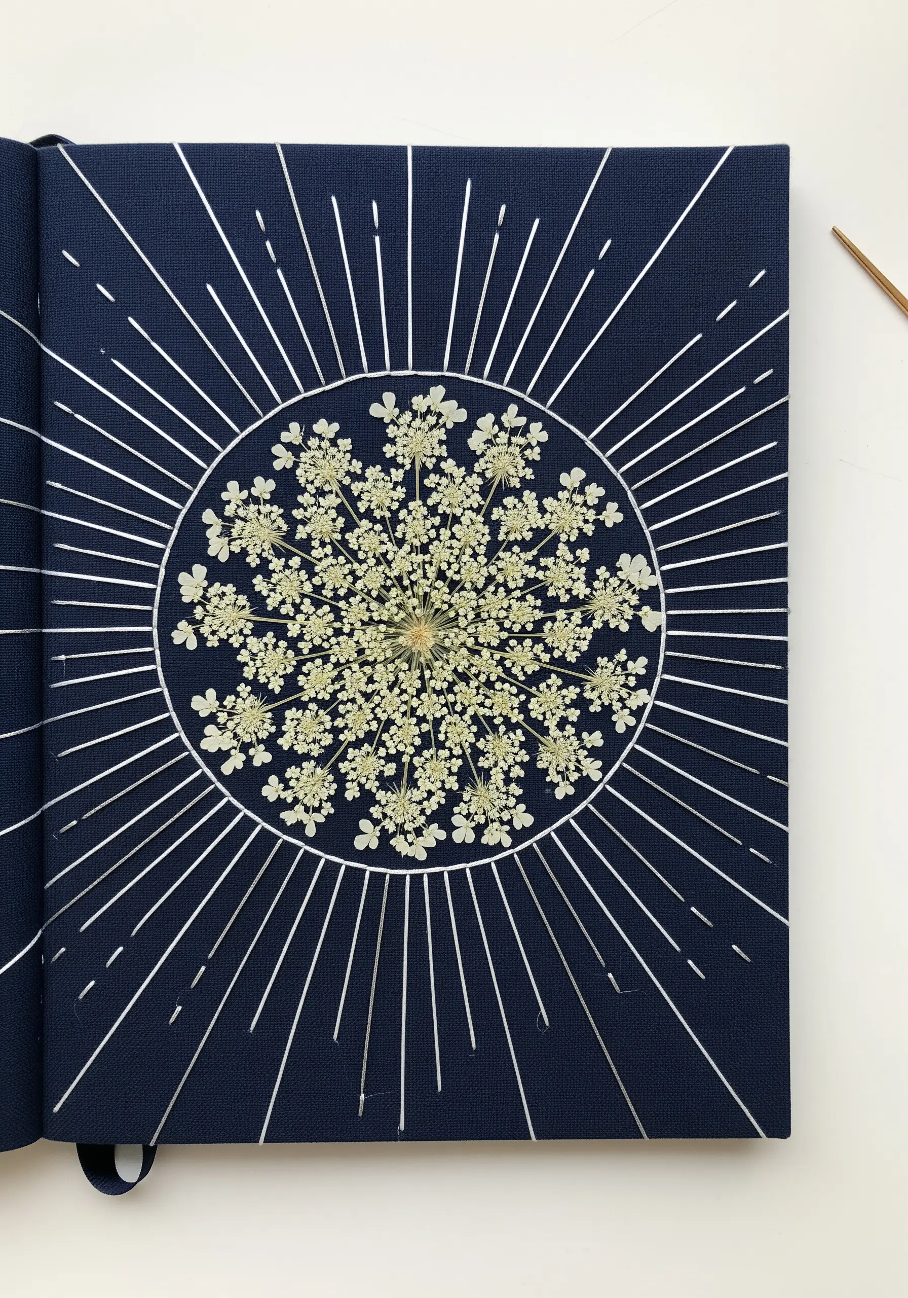 A pressed Queen Anne's lace flower with radiating lines of silver metallic thread.