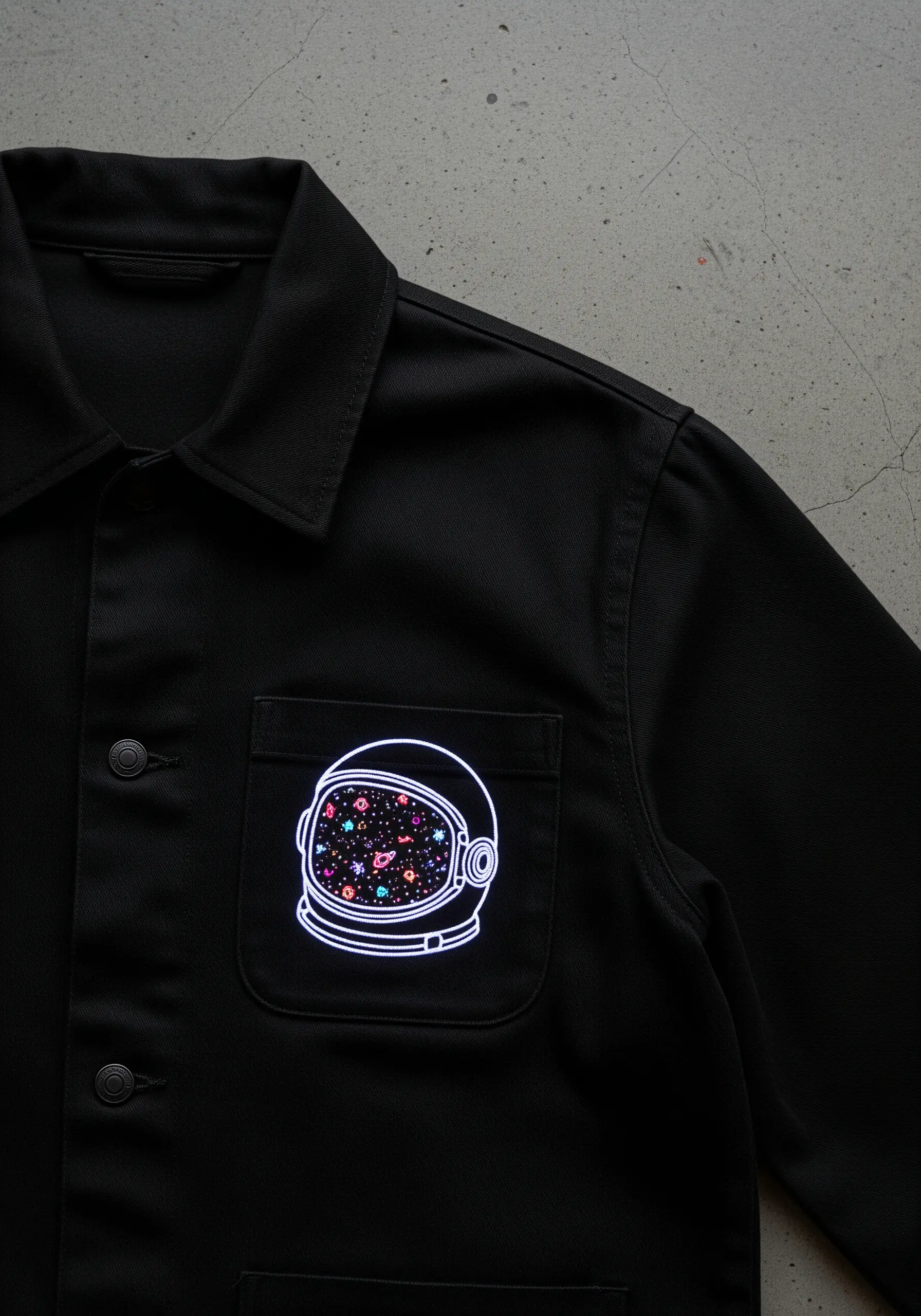 An astronaut helmet outline on a jacket pocket, filled with a colorful galaxy of tiny stitches.