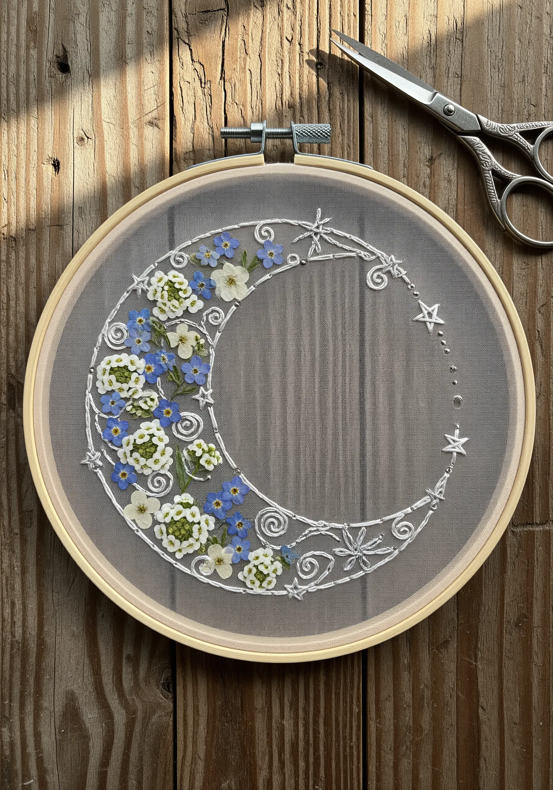 Pressed flowers and stars stitched in white on sheer tulle within a wooden embroidery hoop.