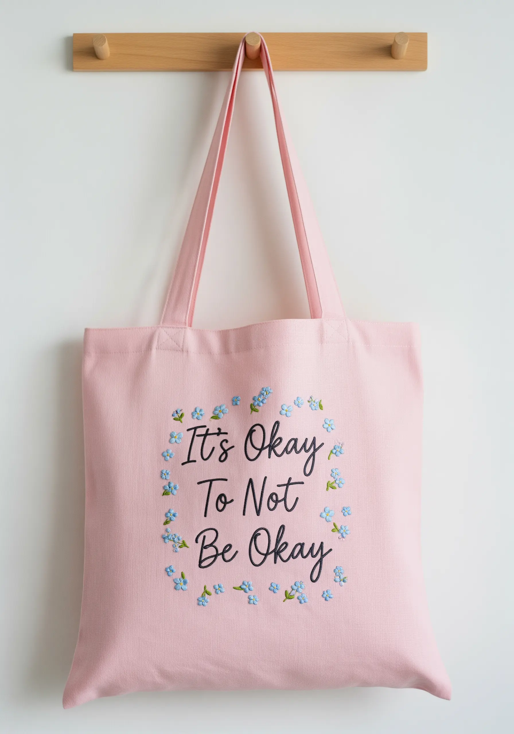 Embroidered quote 'It's Okay To Not Be Okay' circled by forget-me-nots on a pink tote.