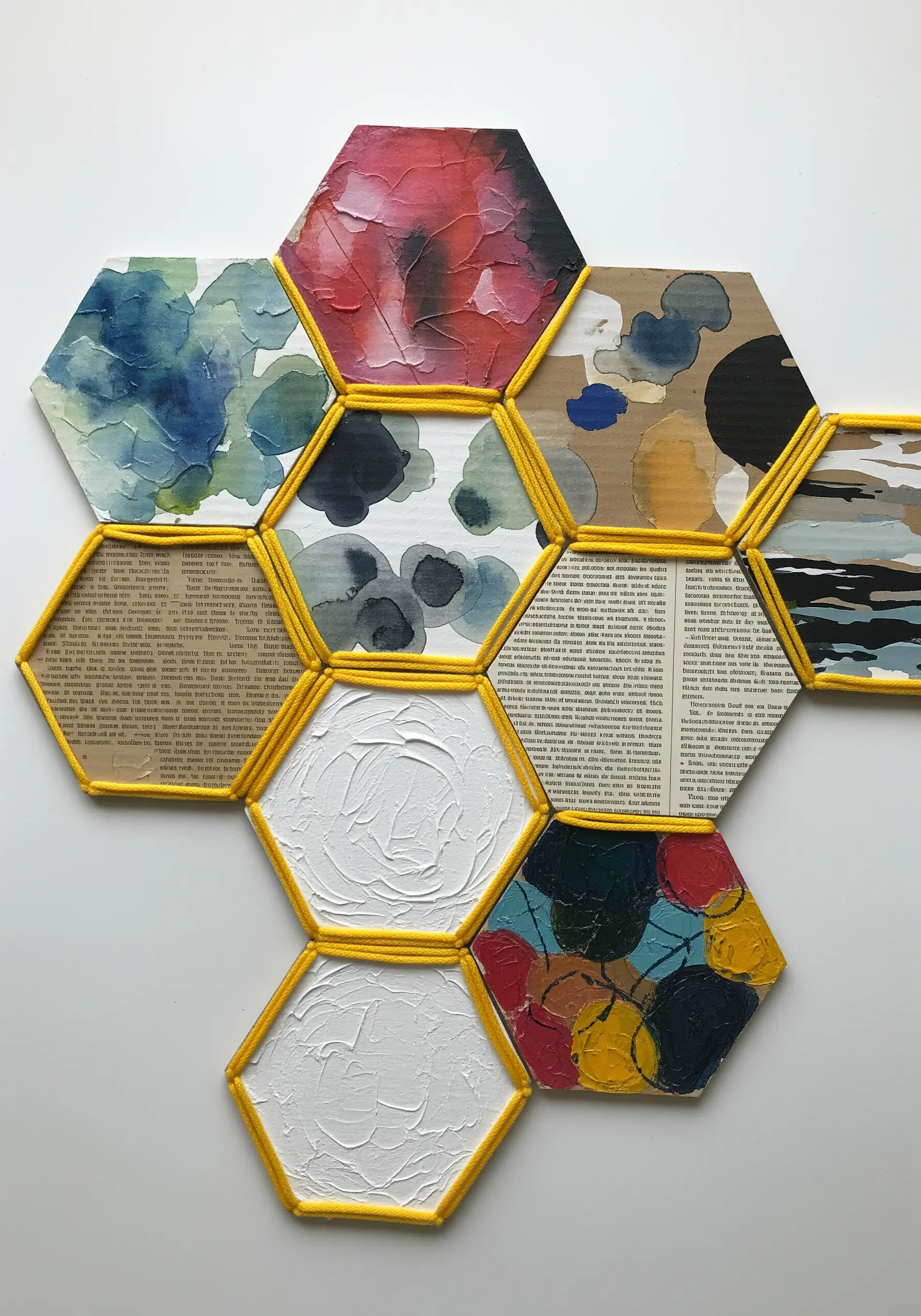 A mosaic of hexagonal cardboard tiles decorated with paint and paper, their edges wrapped in yellow yarn.